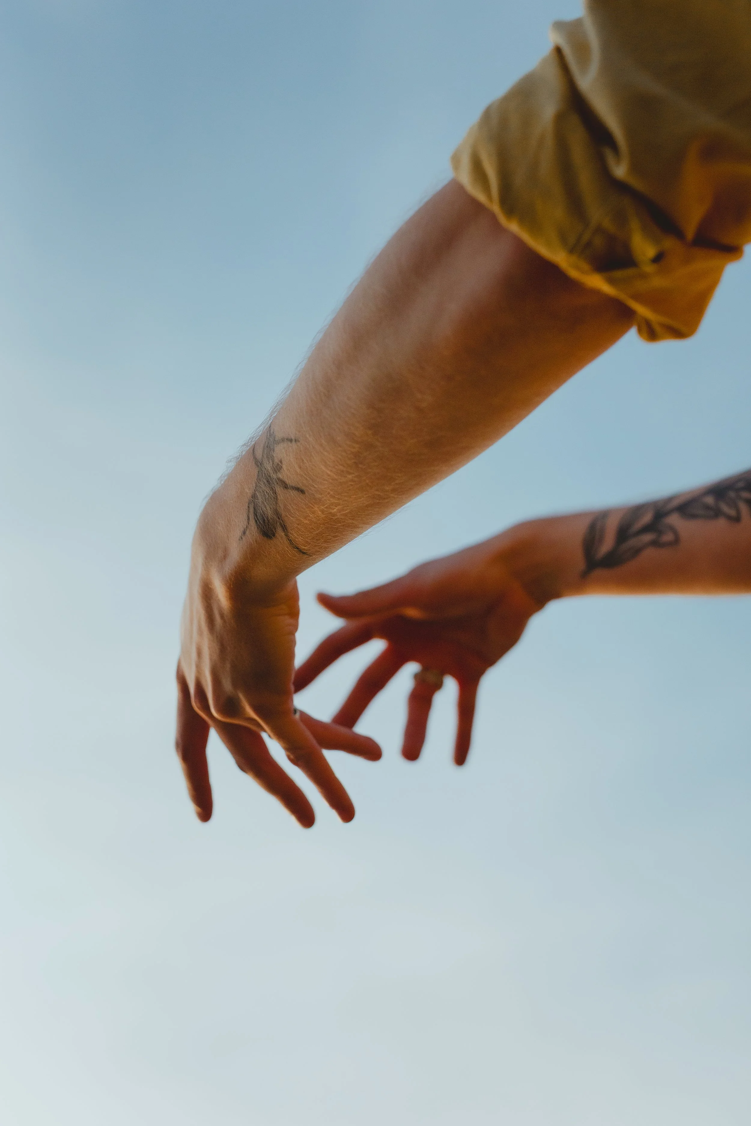 Cinematic softly lit photograph of two hands reaching towards light with a blue backdrop with tattoos and a yellow shirt in Oulton Broad Suffolk 