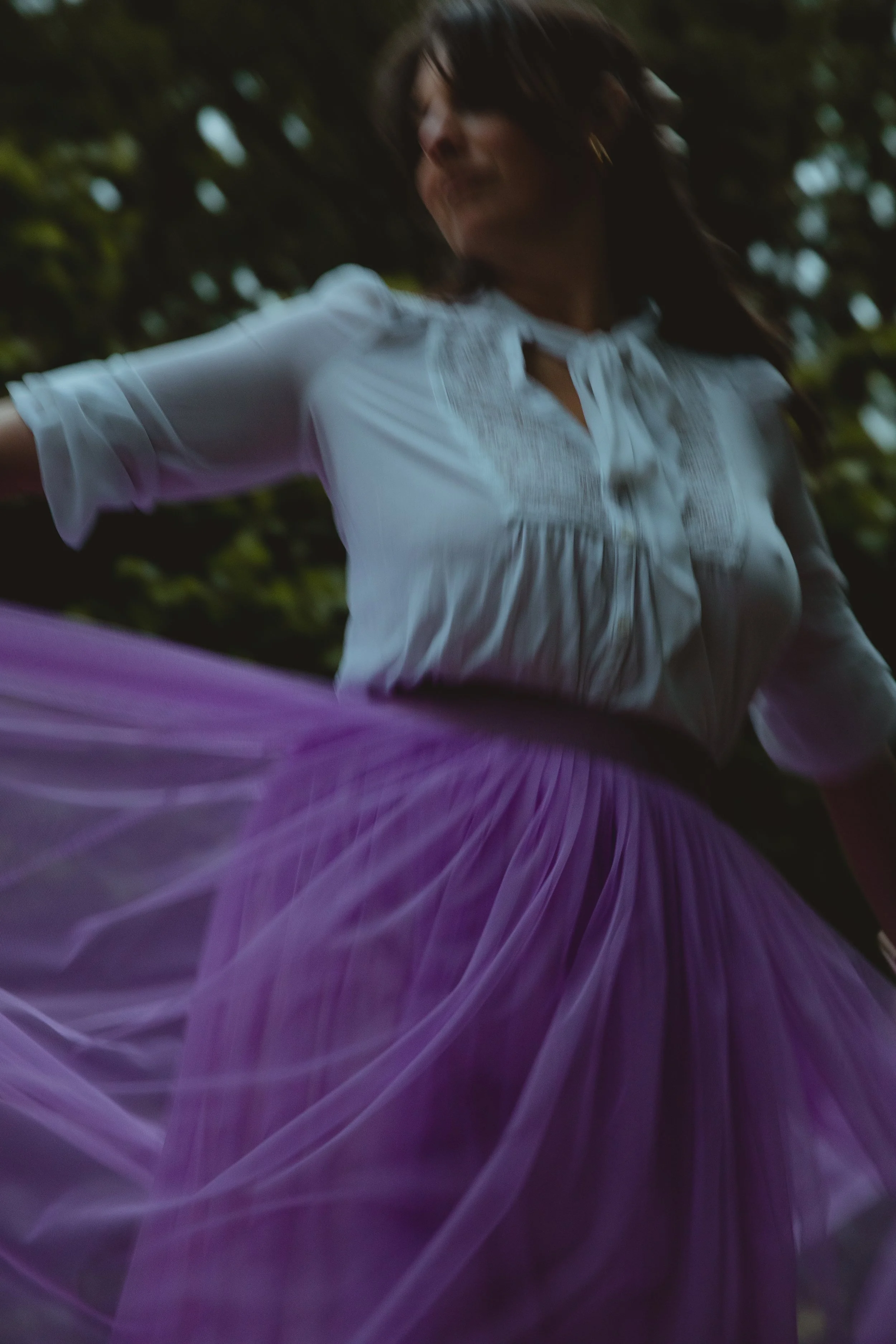 Soft artistic editorial image of a woman in a white blouse and purple skirt spinning in low light blurry in Somerleyton Suffolk 