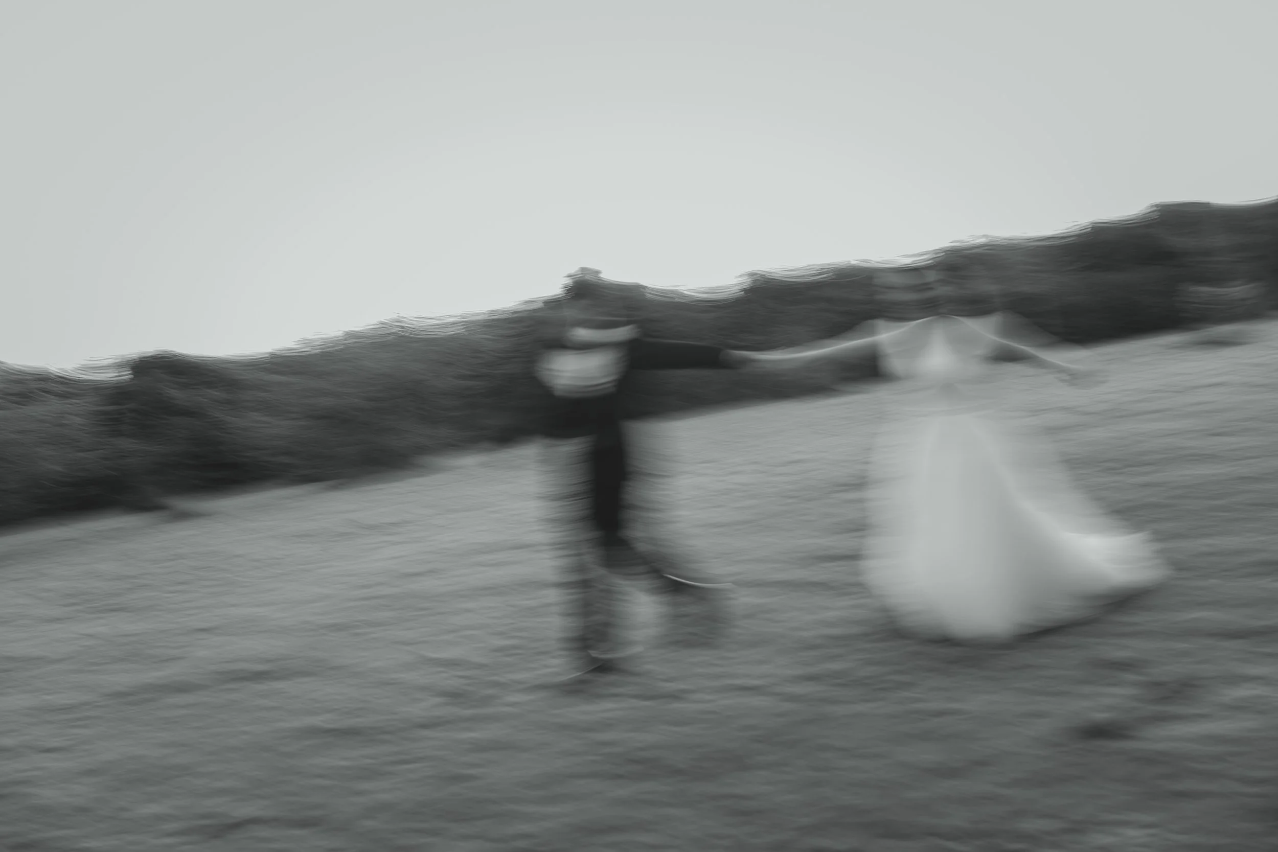 Editorial artistic abstract soft focus black and white photograph of couple holding hands running across a field at golden hour lowestoft suffolk 