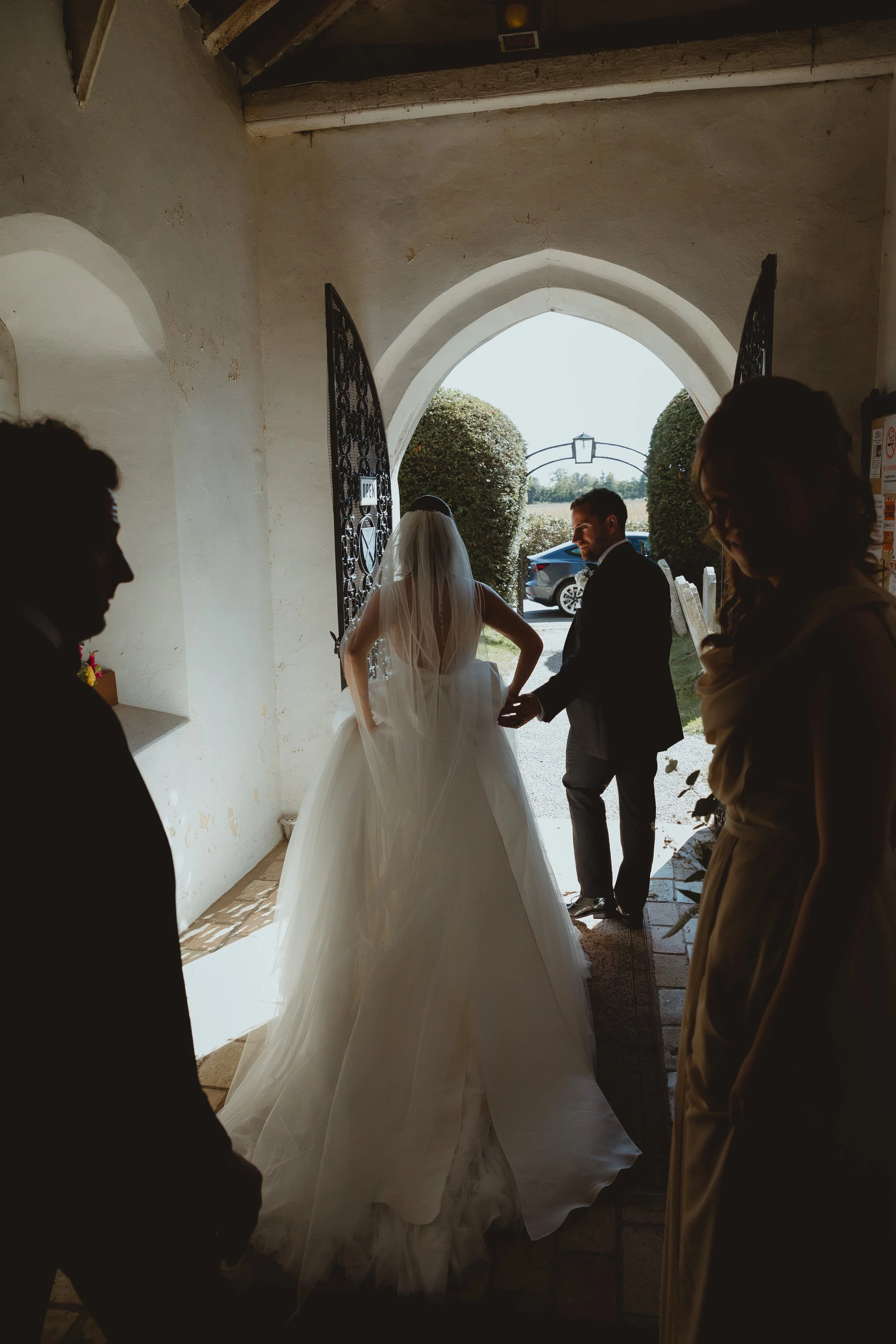 Documentary shot in church of bride and groom racing out of a whitewashed church into a bright garden with light softly on the veil in Blundeston Lowestoft Suffolk 