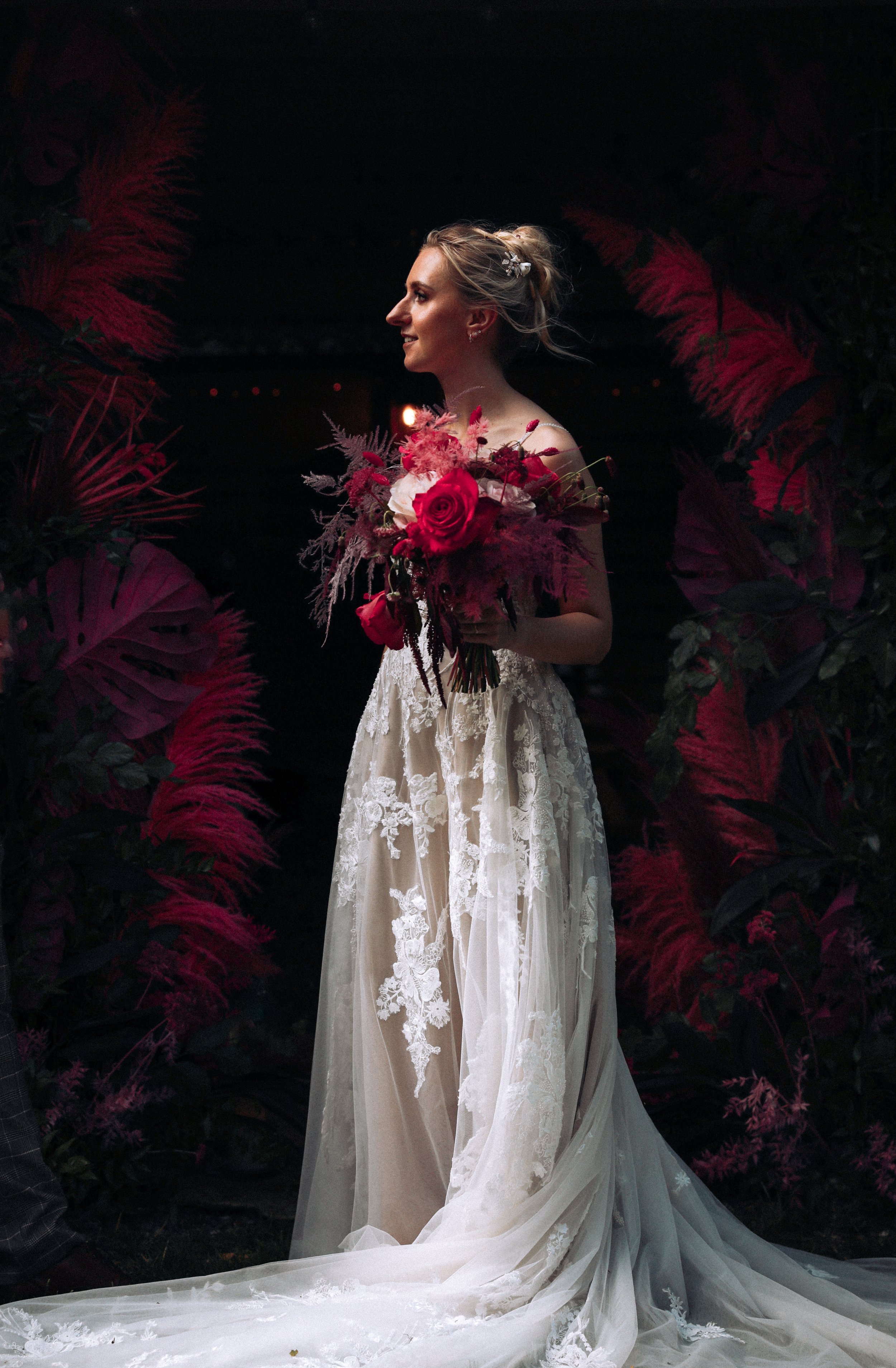 Editorial fine art contrasted dark cinematic pink portrait of bride softly lit amongst pink roses and ostrich feathers at outside wedding at Upthorpe Wood Bury St. Edmunds Suffolk 