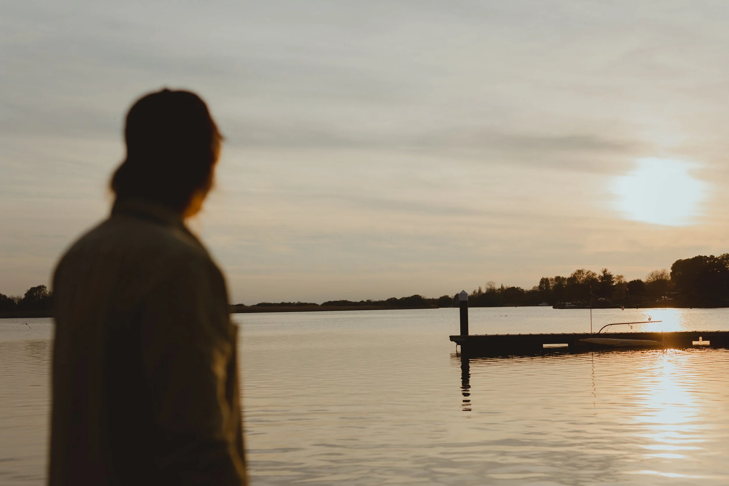 Wide shot cinematic landscape shot of male yoga teacher in silhouette looking out onto the sunset at Oulton Broad Suffolk Norfolk Broads 