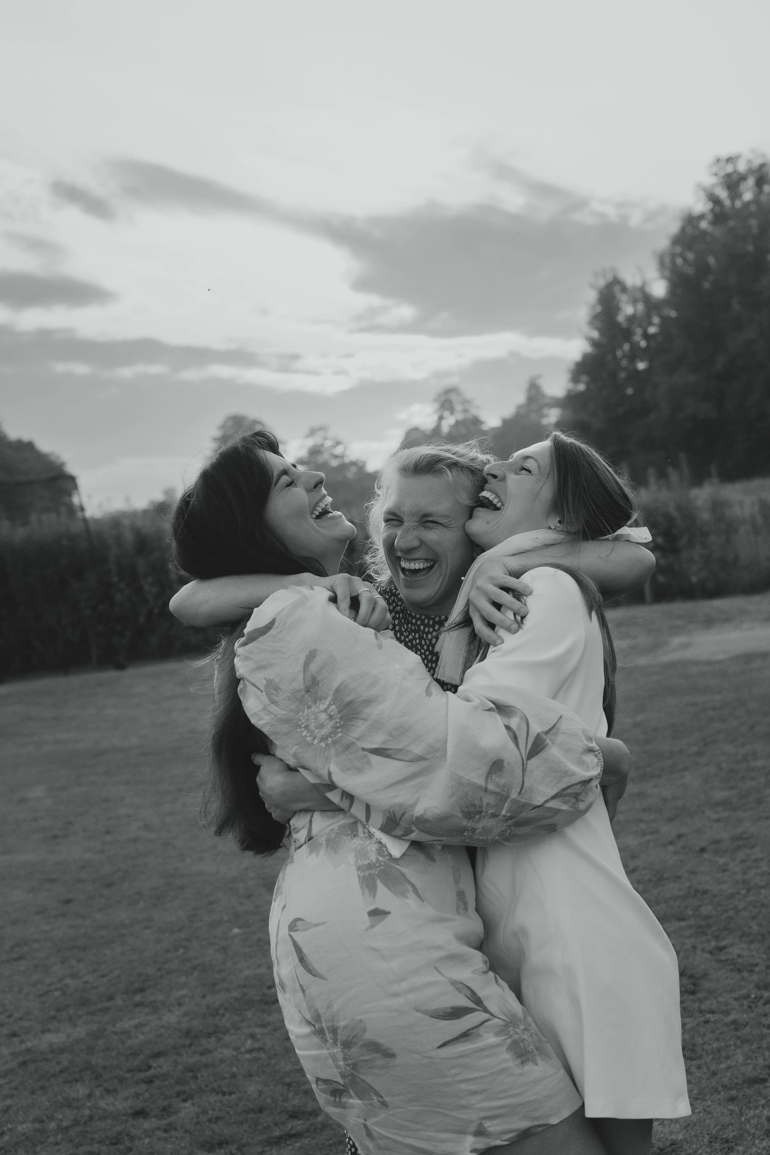 Emotive black and white documentary image of bride and two bridesmaids hugging each other in joy at the reception at Sudbourne Hall Cricket Club Orford Suffolk Coast 