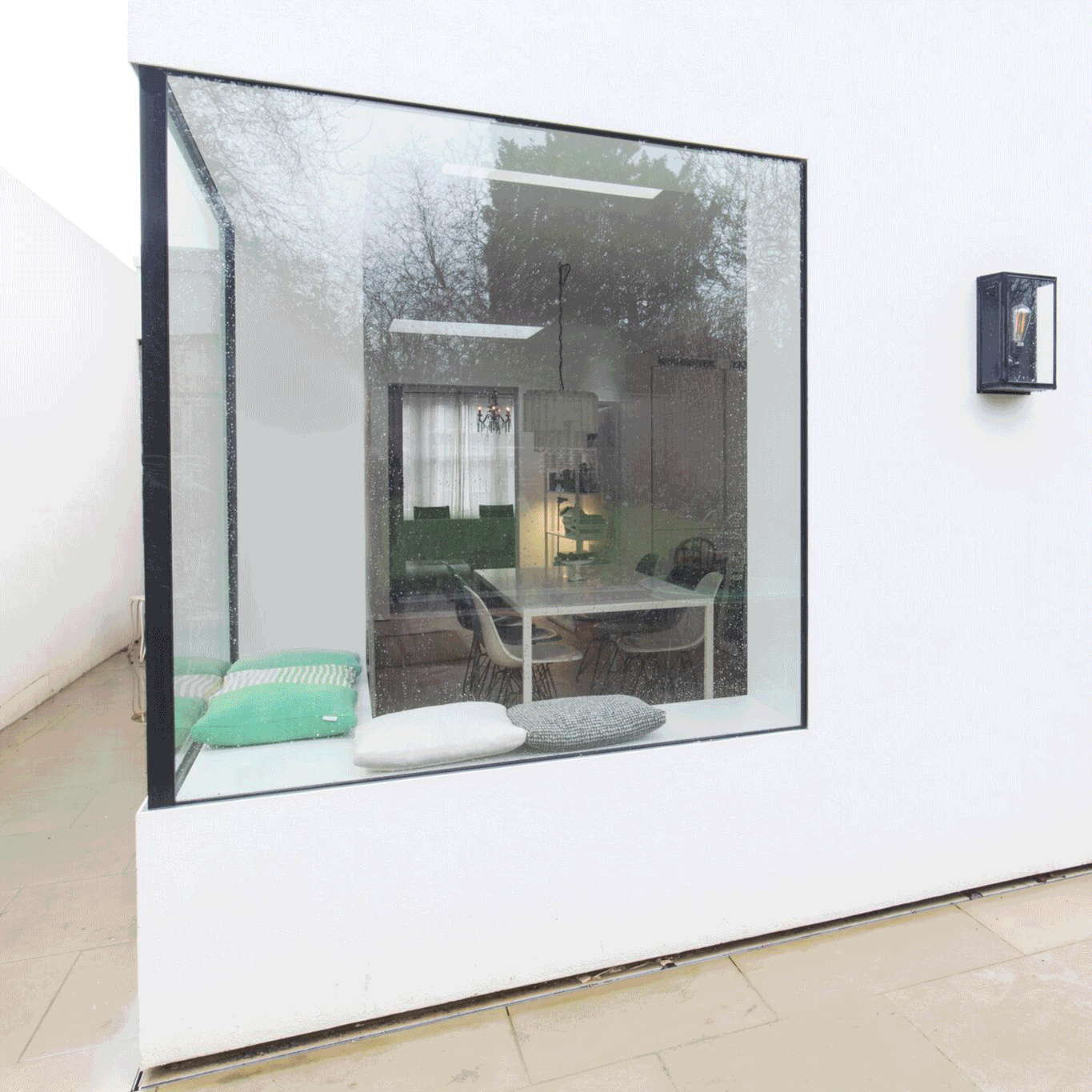Interior view of a modern house through a large glass window, with a dining area and chairs inside