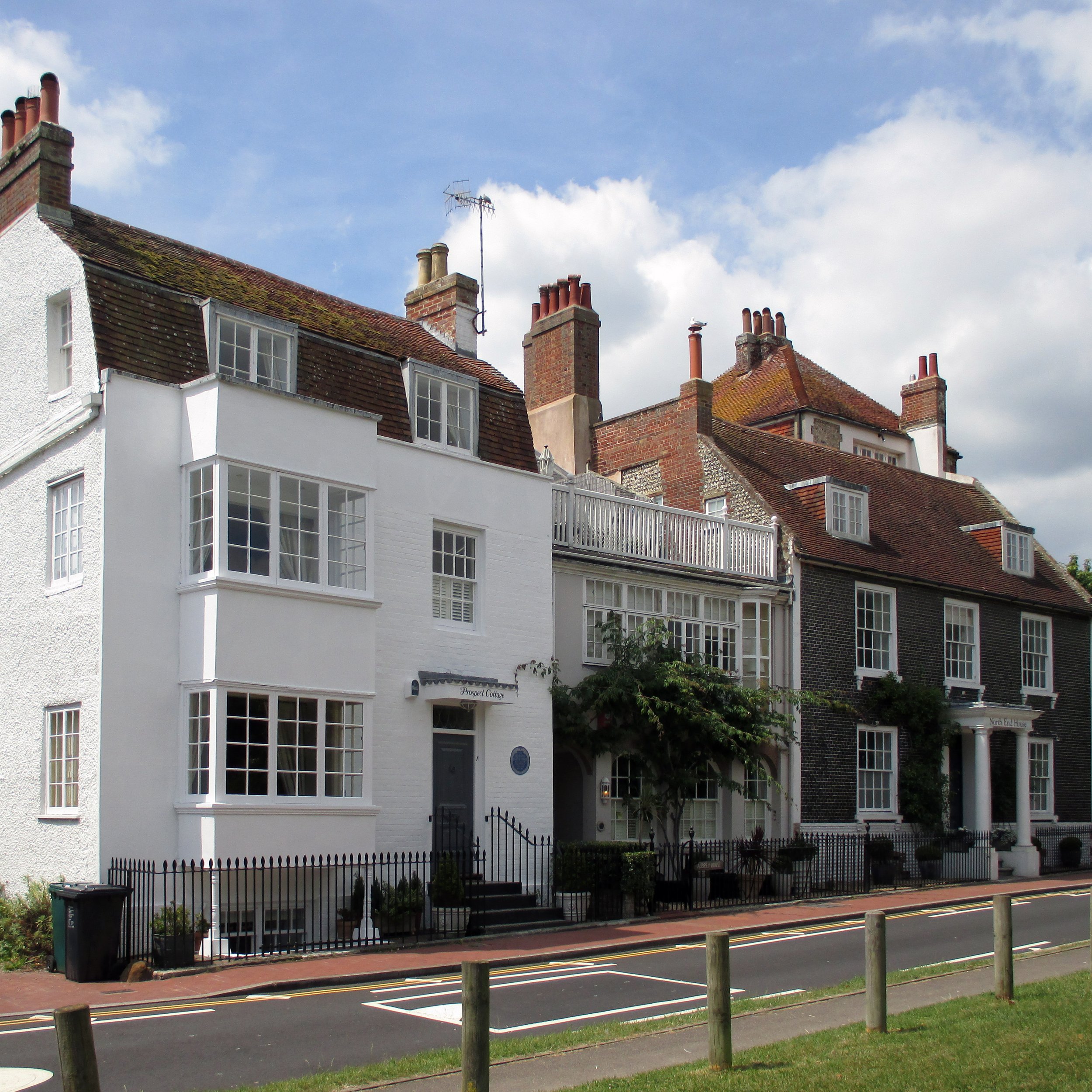 A row of traditional houses with brick and stucco facades, multiple chimneys, and pitched roofs under a partly cloudy sky.