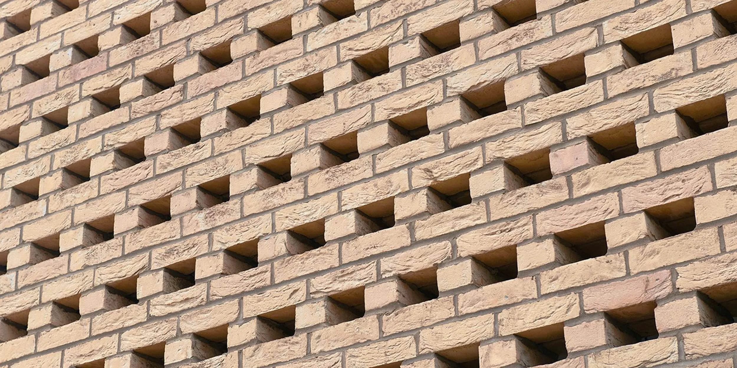Close-up of a beige brick wall with a grid of small square recesses.