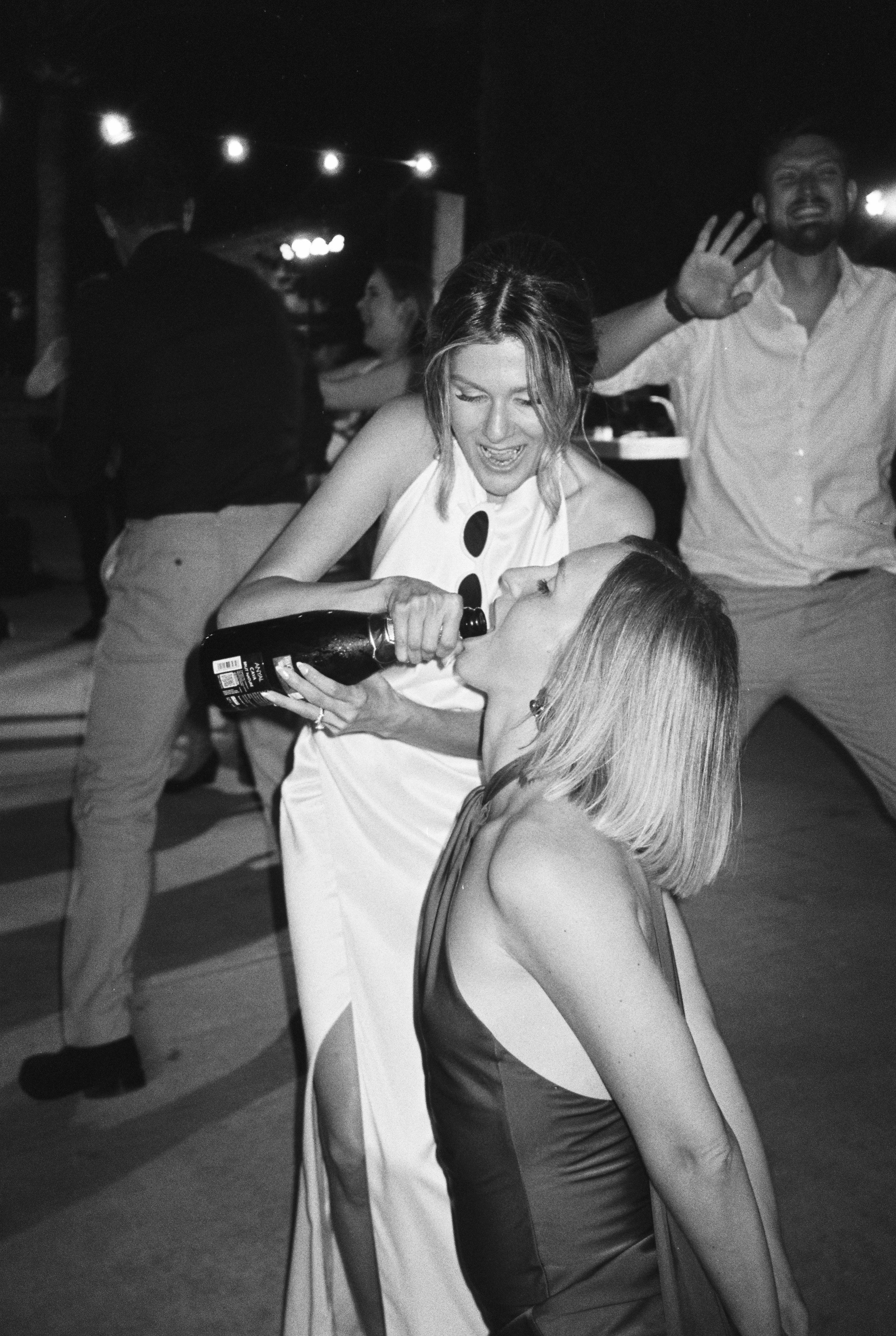 People dancing at a party, with a woman pouring champagne into another woman's mouth.