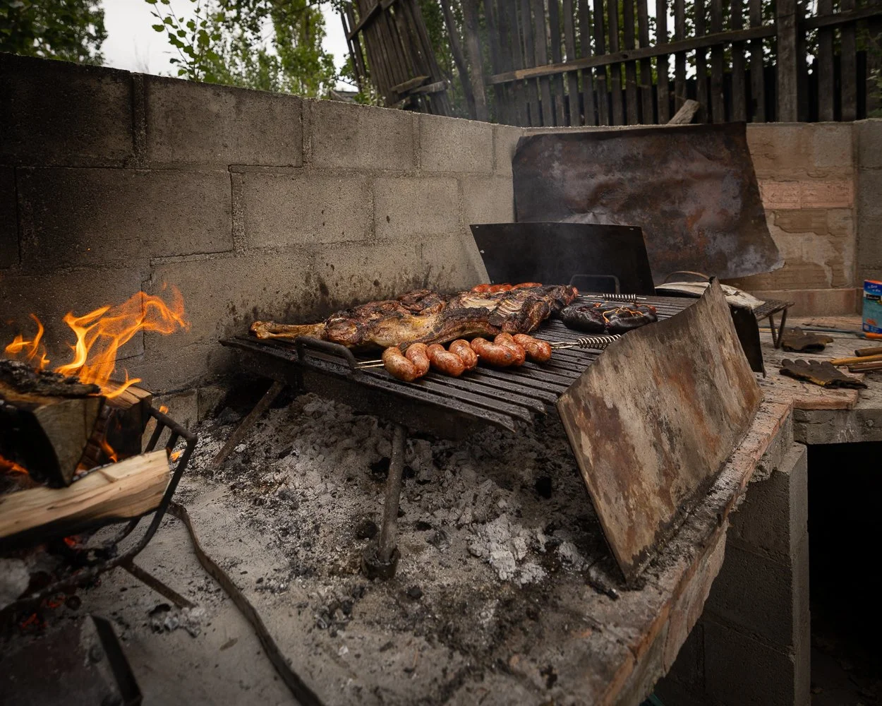 Grill med kød og pølser, mens der er åben ild på en udendørs grillplads med sten og mursten.