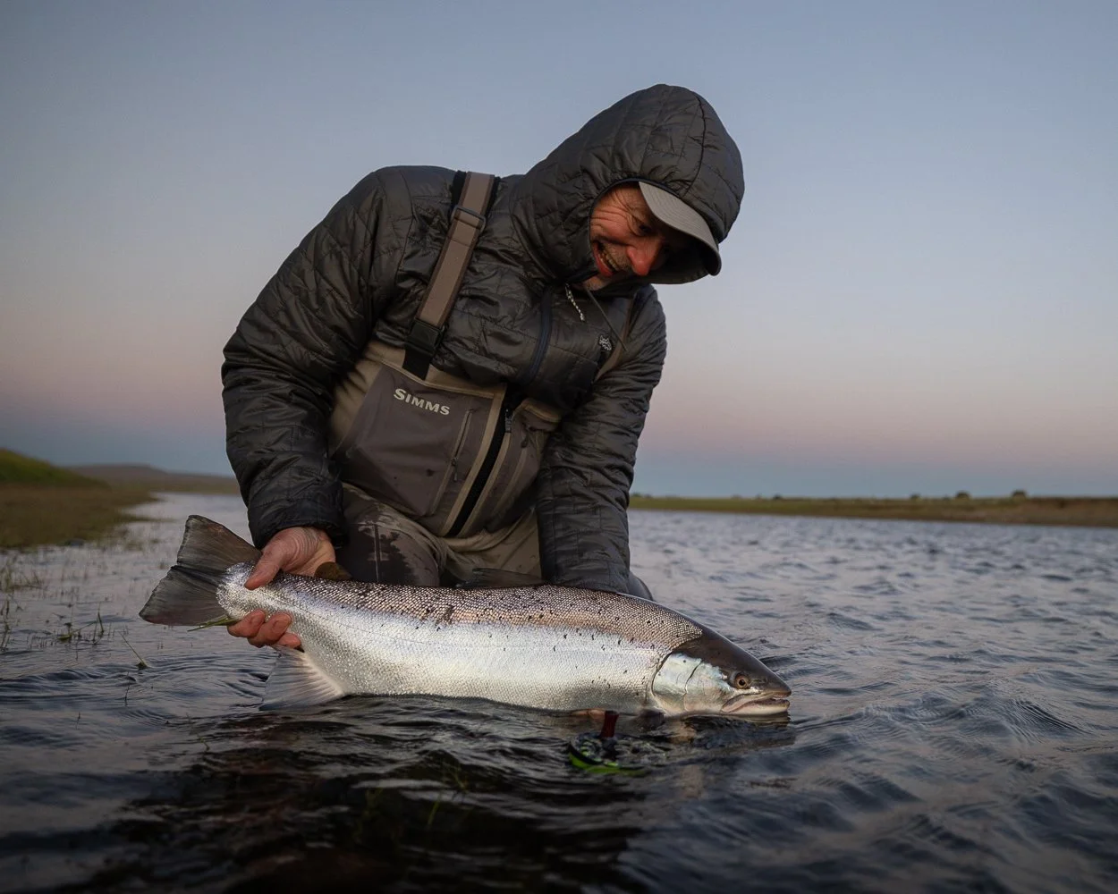 Mand holder en stor fisk i vandet ved solnedgang.