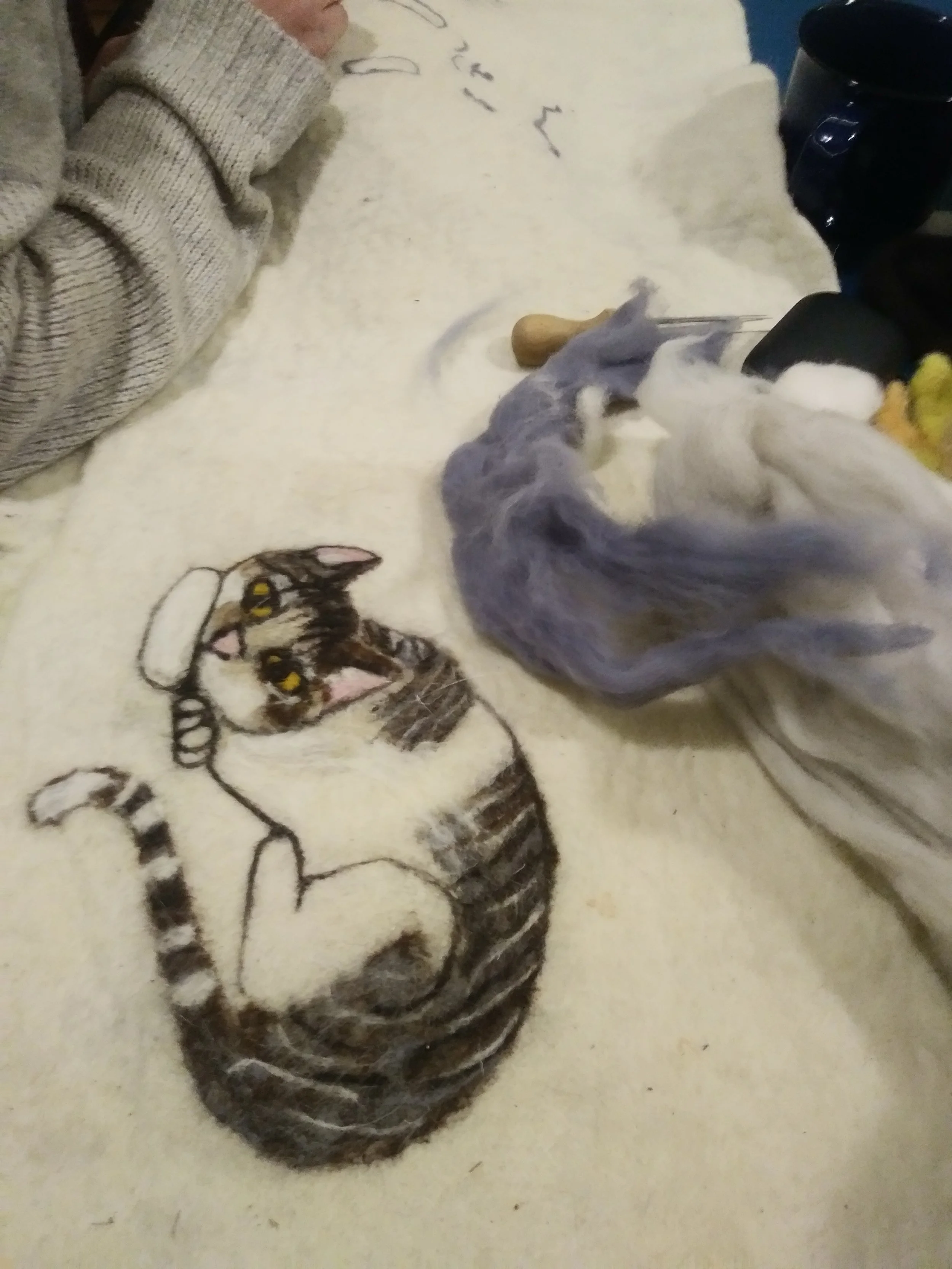A handmade felted kitten on a big felt sheet.