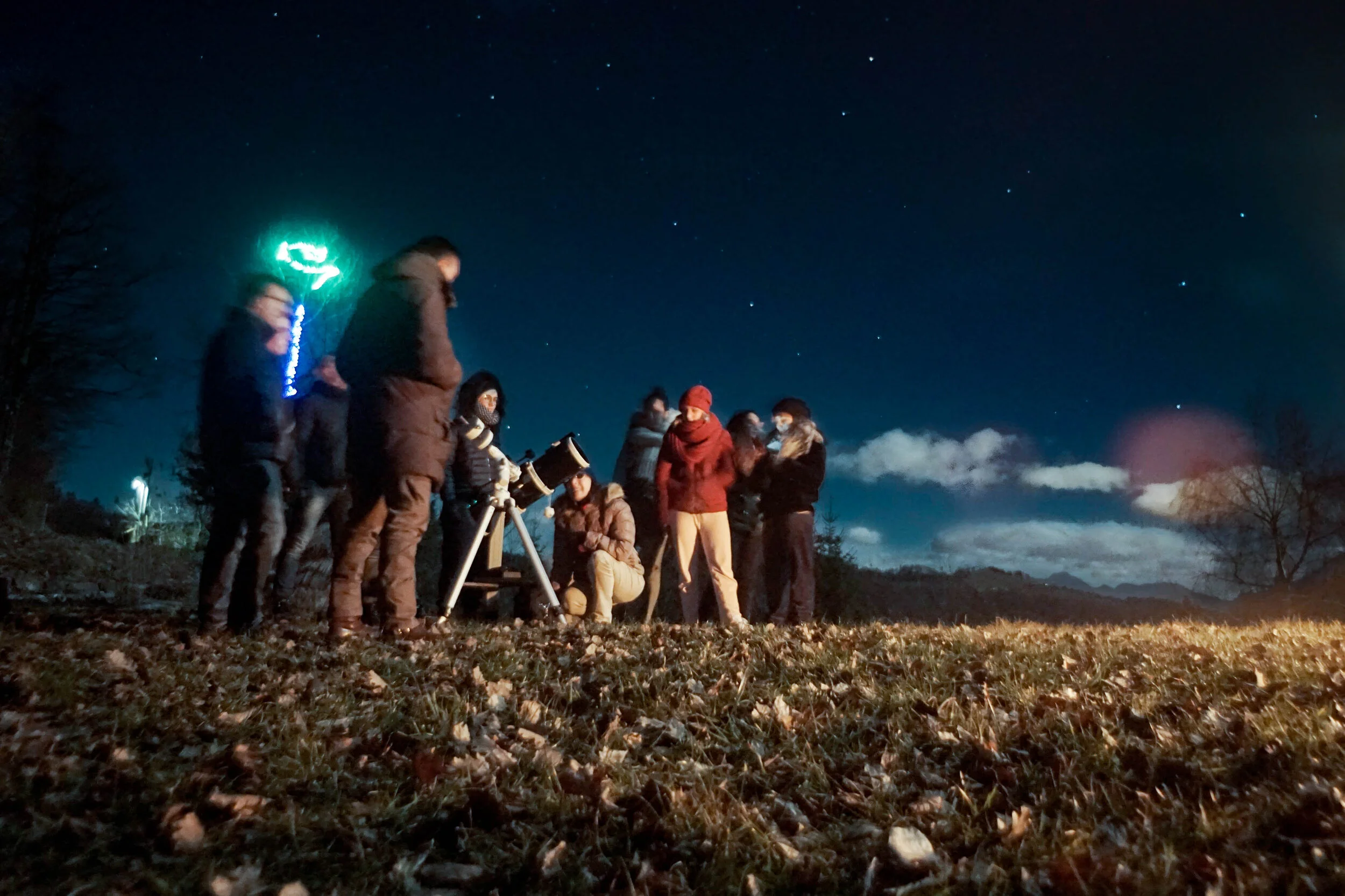 A group of people gathered around a telescope, looking at the night sky