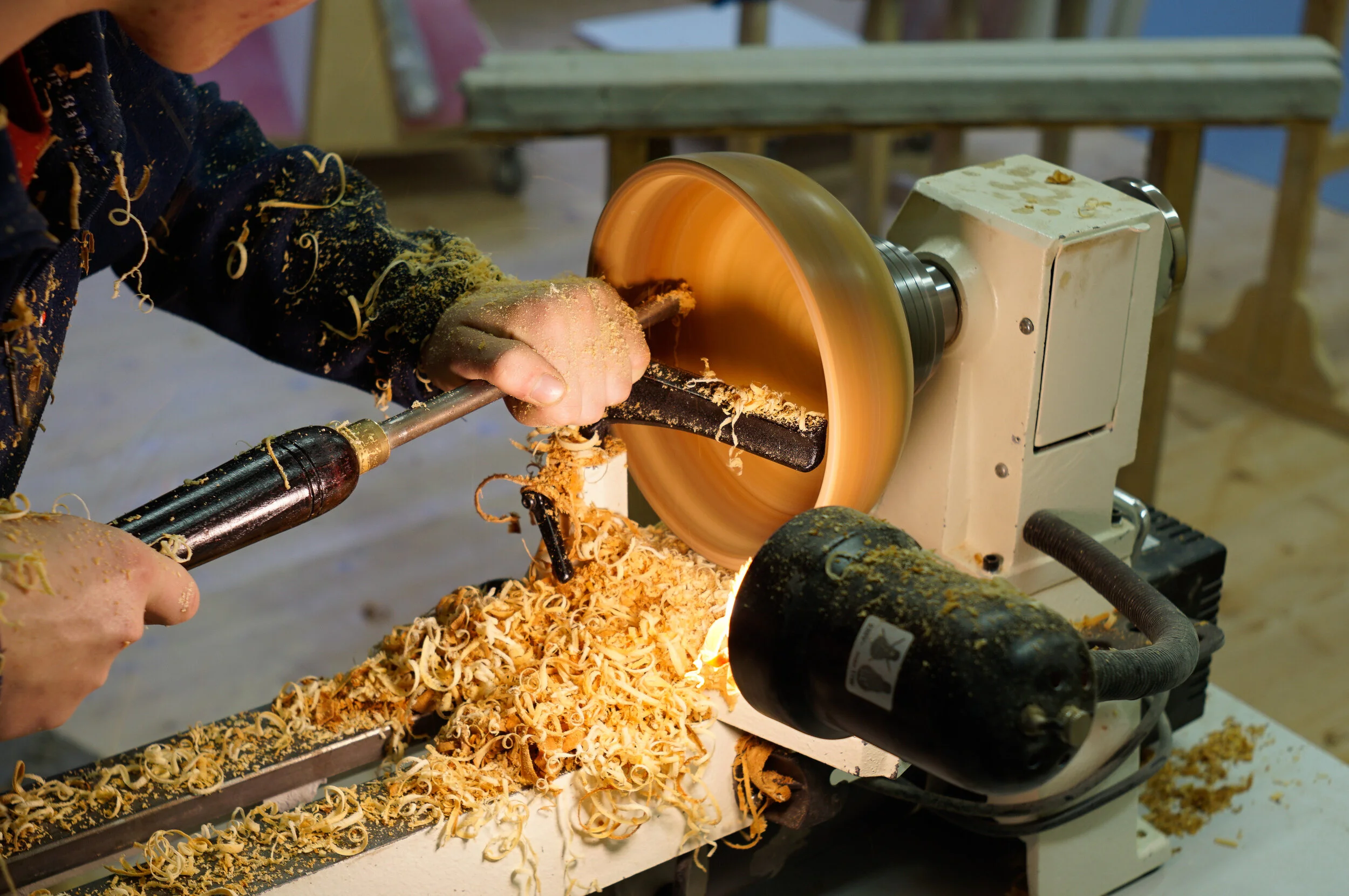 Person turning a wooden bowl on a lathe.
