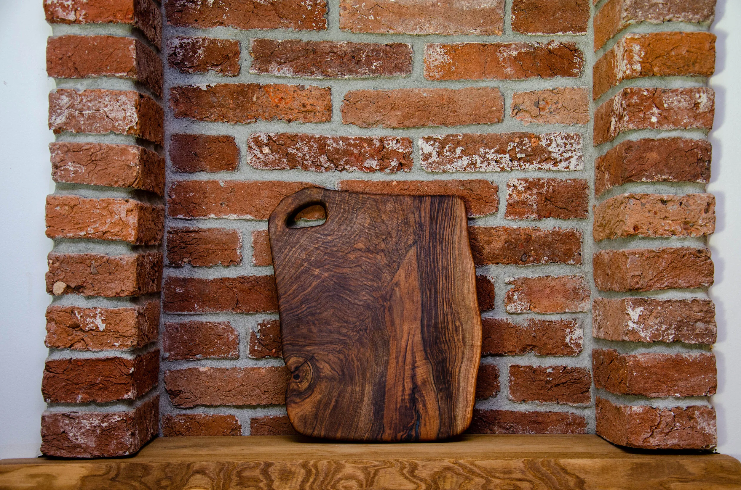 A wooden cutting board leaning against a brick wall.