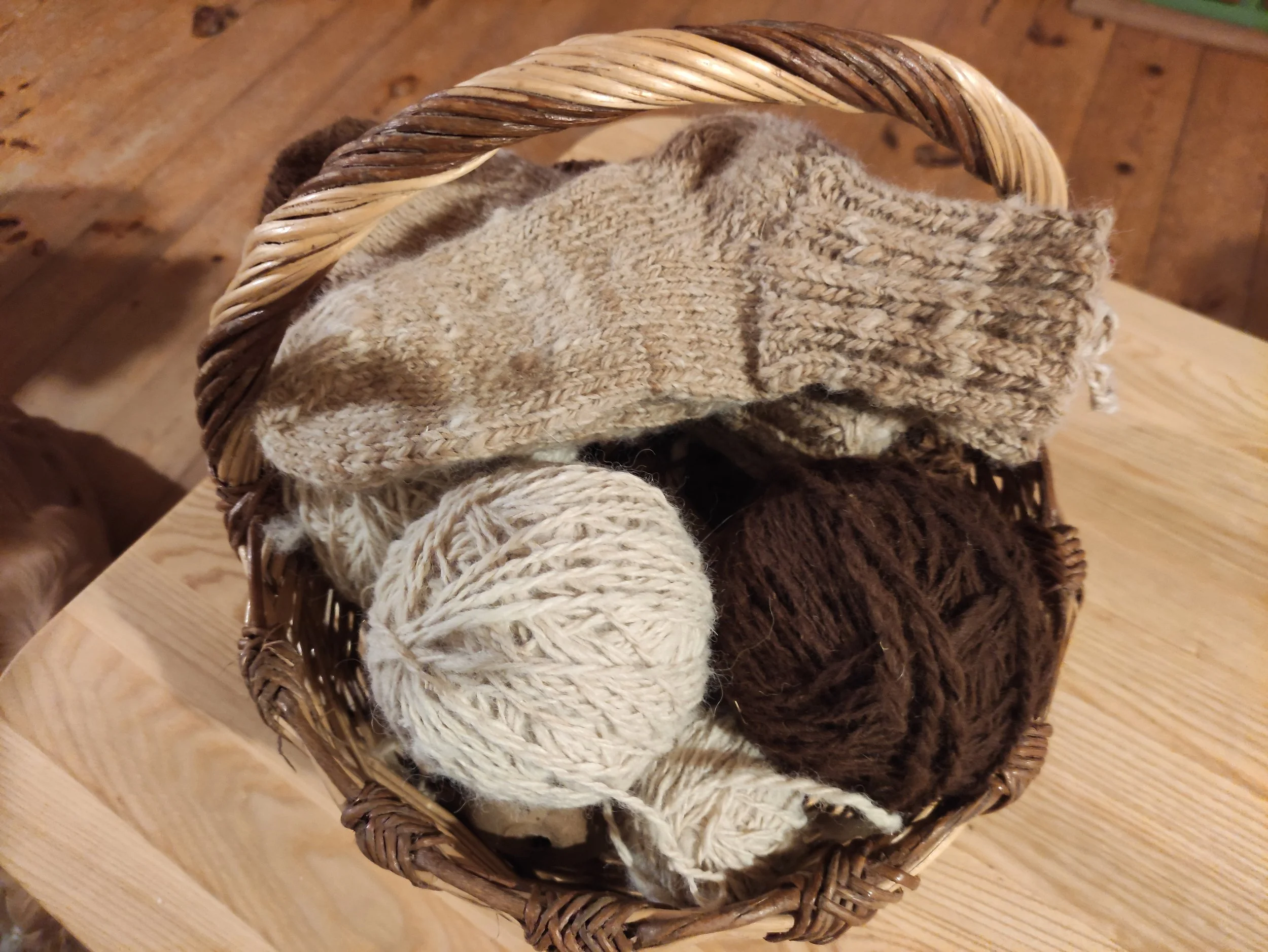 Wicker basket containing brown alpaca yarn balls and socks on a wooden surface.