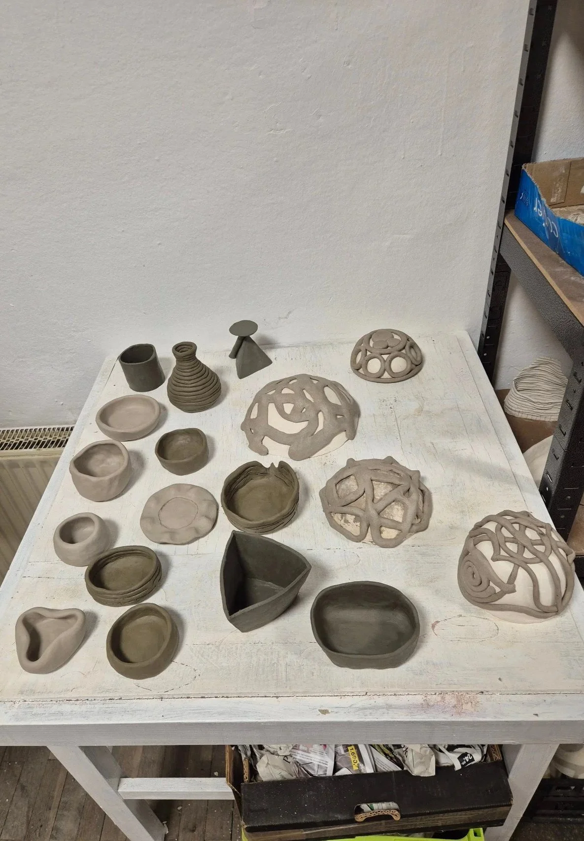 Ceramic pottery bowls, vases, and decorative sculptures on a white table in a pottery studio.