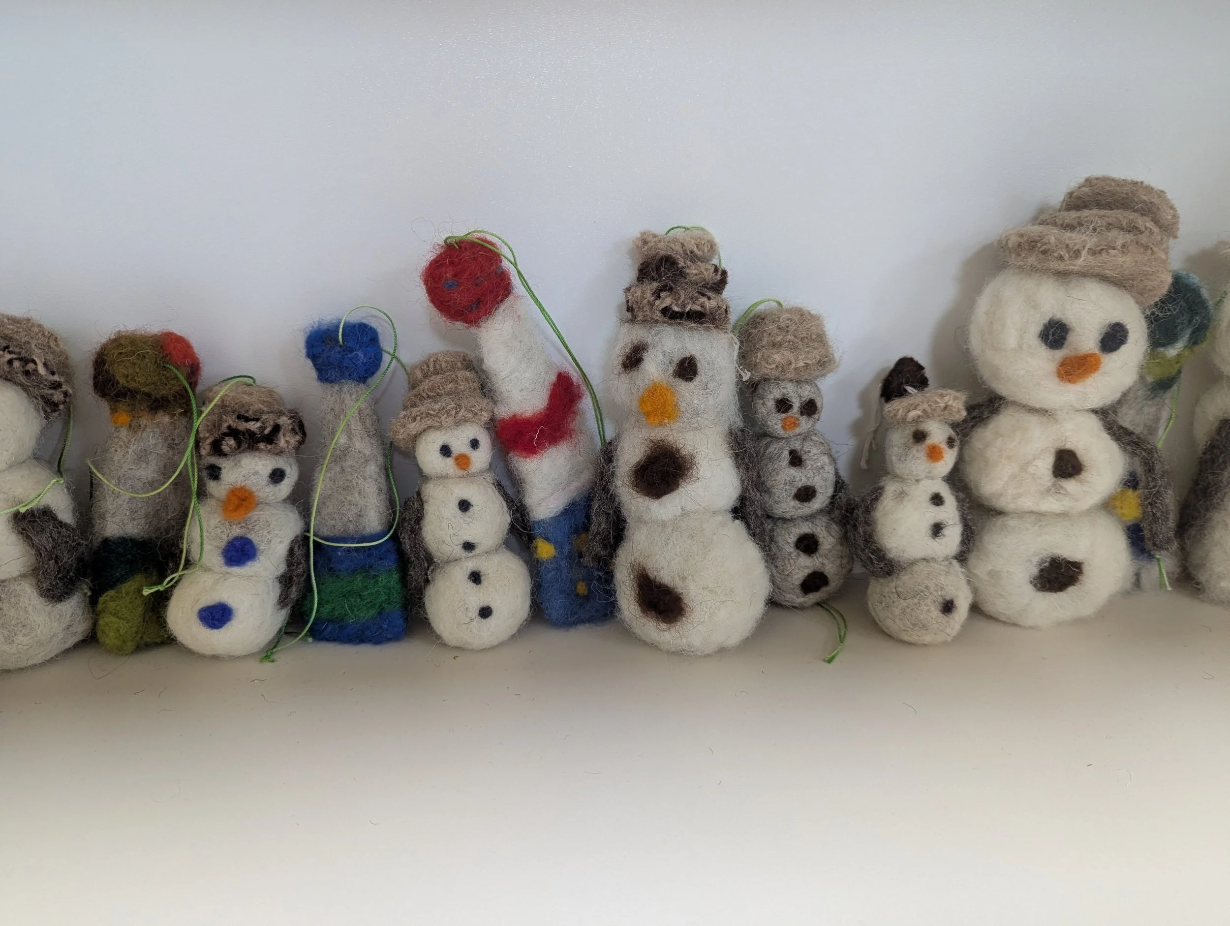 Several small felted snowpeople with different colored scarves and hats lined up against a wall, made by schoolchildren.