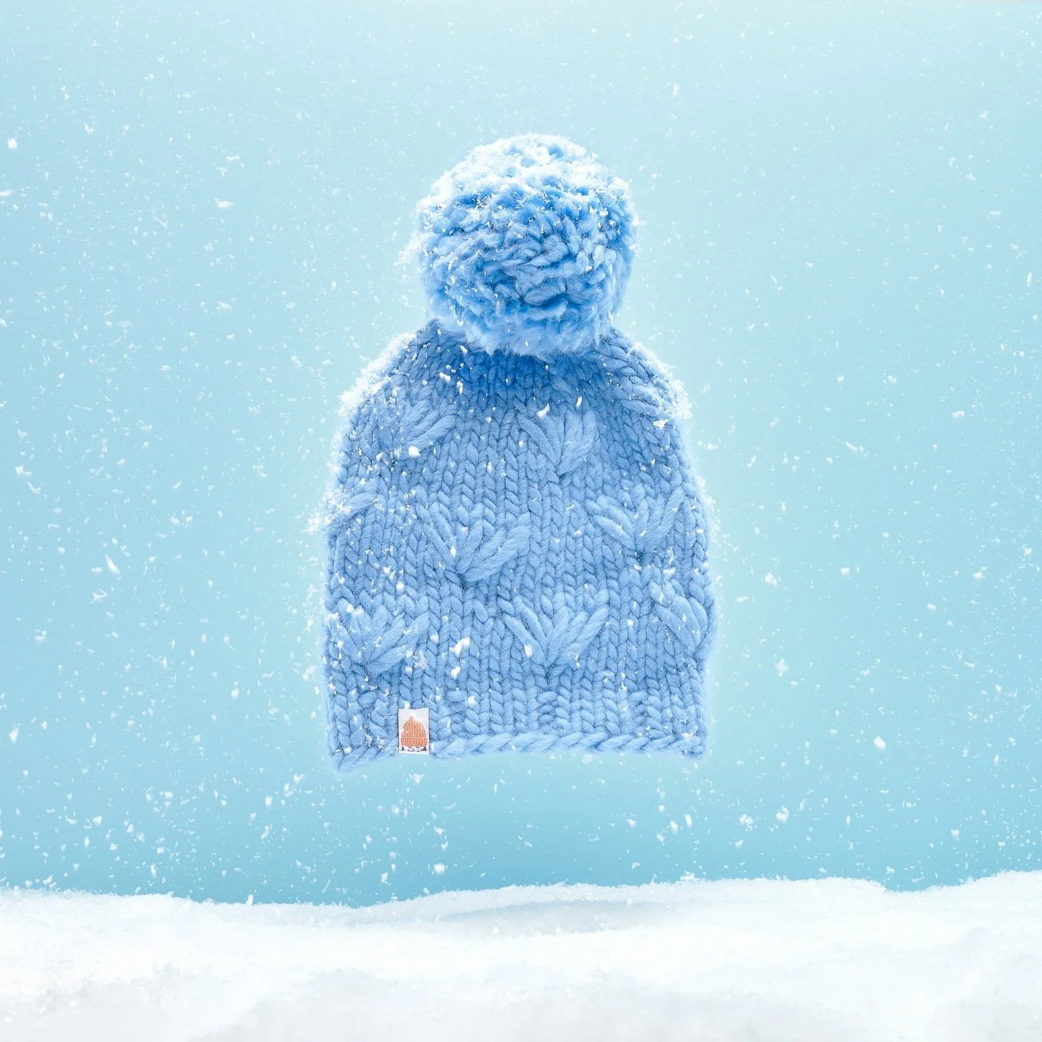 A knitted winter hat with a pom-pom on top is floating in the air against a snowy winter background.