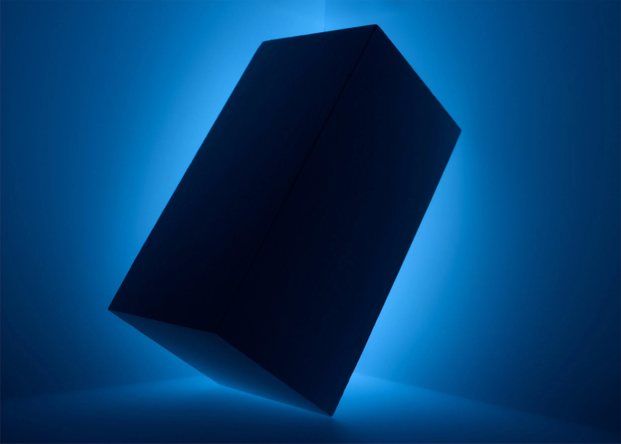 A dark rectangular box with textured surface is illuminated from behind, casting a shadow and creating a glow effect on the blue background.