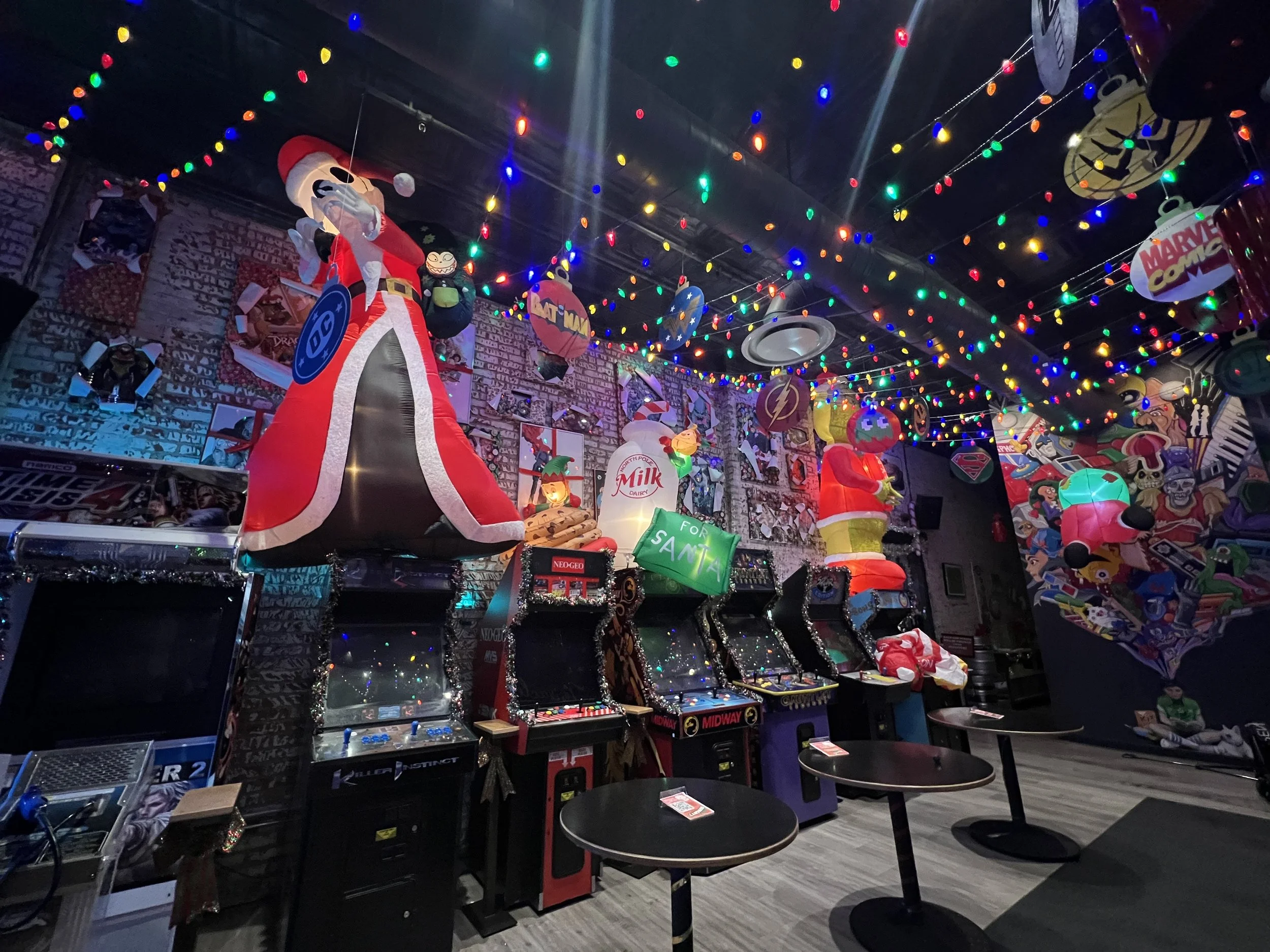 Decorated arcade with Christmas and superhero decorations, colorful string lights, arcade machines, and tables. Mini Boss San Jose.