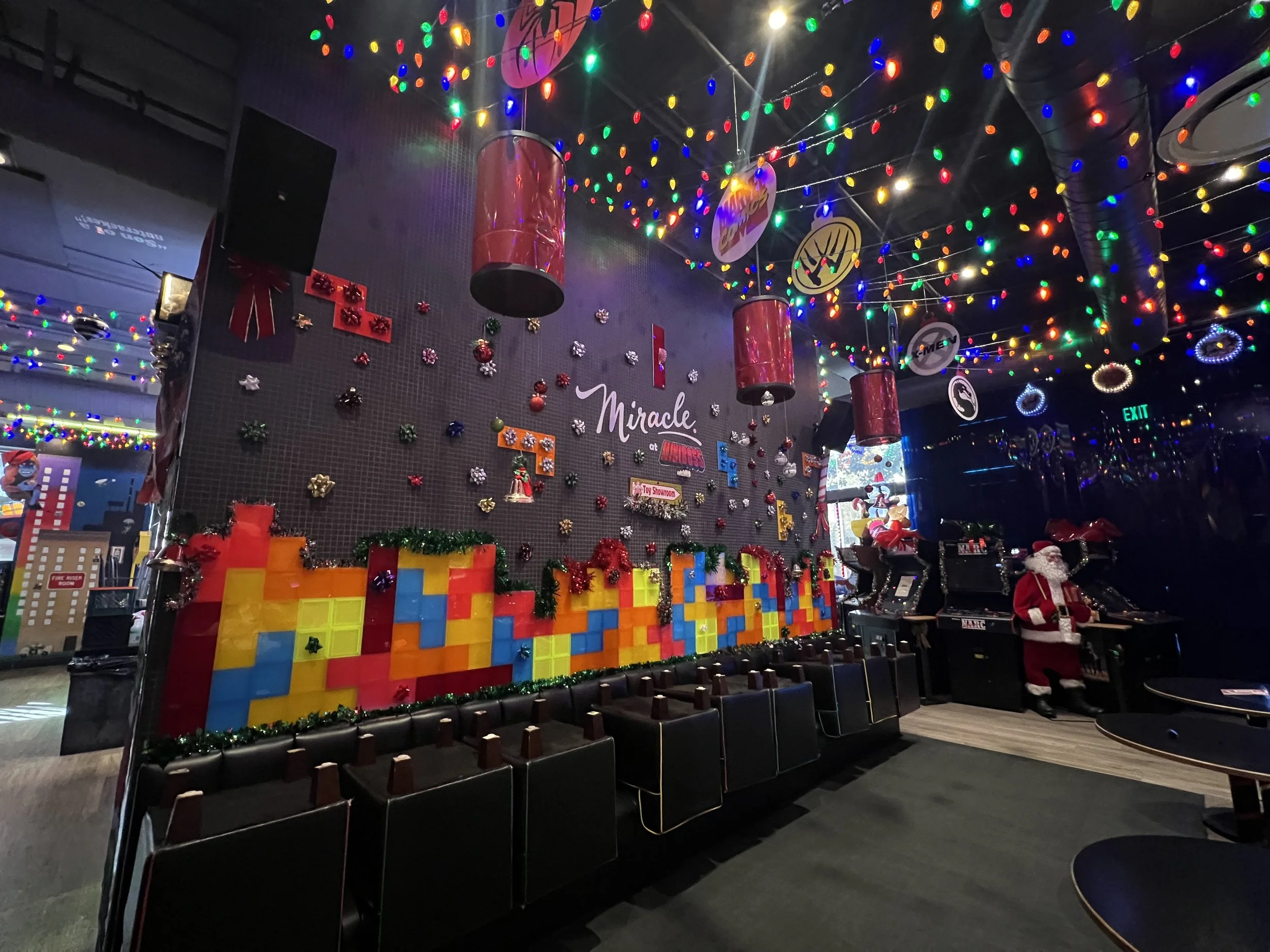 Festively decorated indoor space with Christmas decorations, colorful Christmas lights hung from the ceiling, a wall with tetris blocks, Santa in front of DJ equipment, and Christmas ornaments hanging from the ceiling.