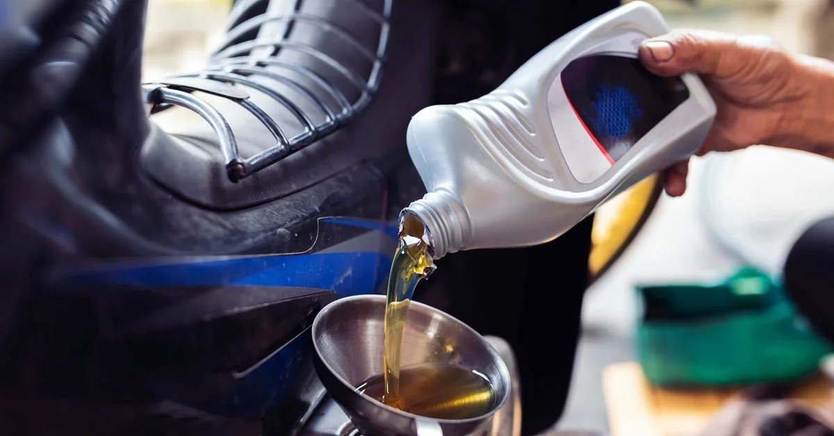 A person is using a funnel to pour a silver bottle of motor oil into the engine bay of a motorcycle.