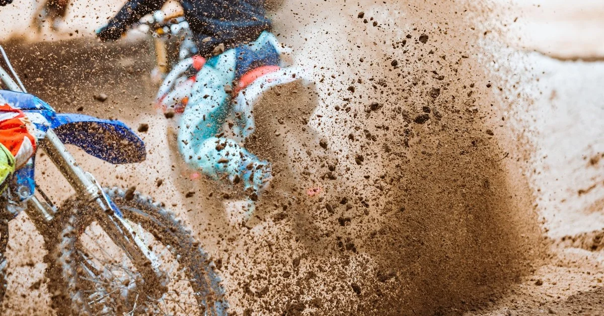 A group of people riding dirt bikes on a motocross track with mud and dirt spraying up into the air behind them.