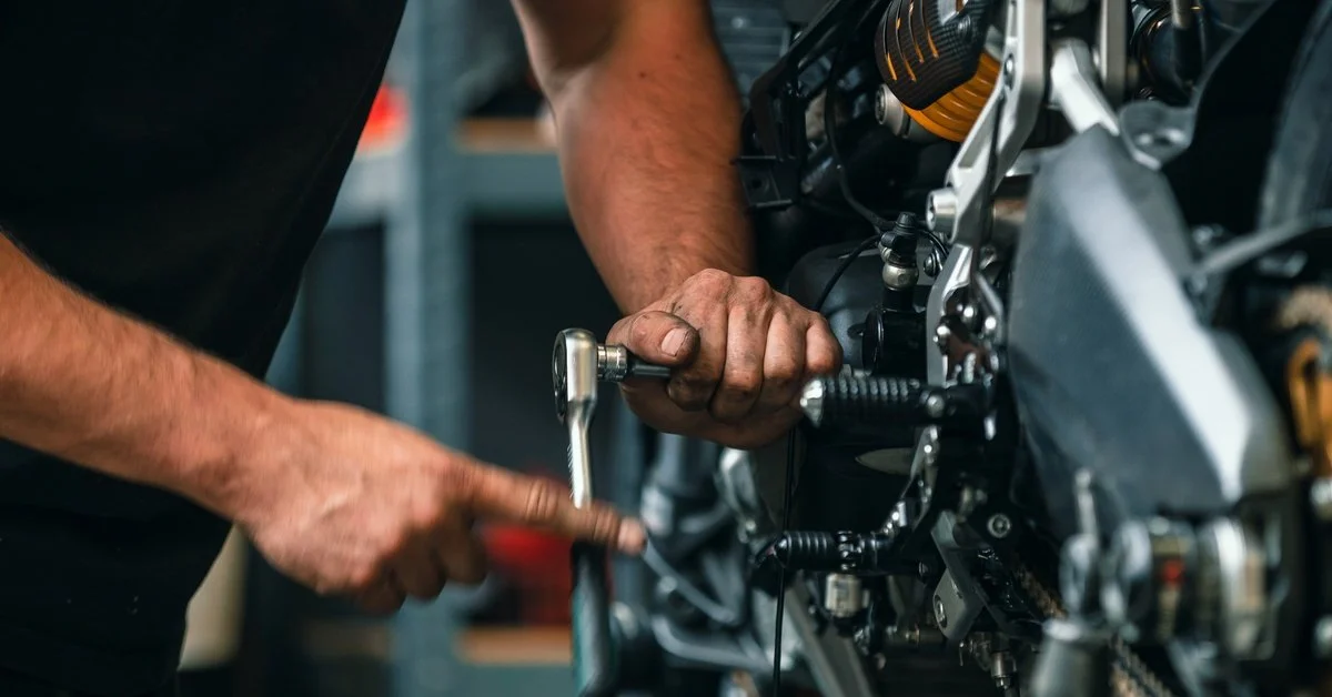 A person wearing a black shirt is using a socket wrench to perform maintenance on the engine of a motorcycle.