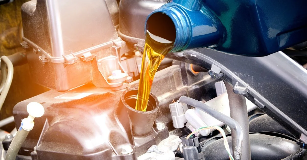 A blue bottle of oil lubricant being poured into the pan of a vehicle inside the engine bay for better performance.