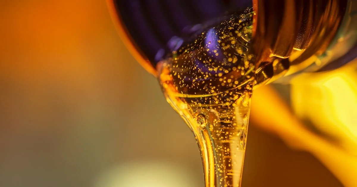 A gold bottle pouring liquid oil lubricant out over a black background as it pools up on an invisible surface.