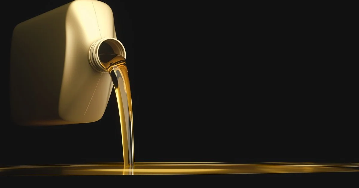 A gold bottle pouring liquid oil lubricant out over a black background as it pools up on an invisible surface.