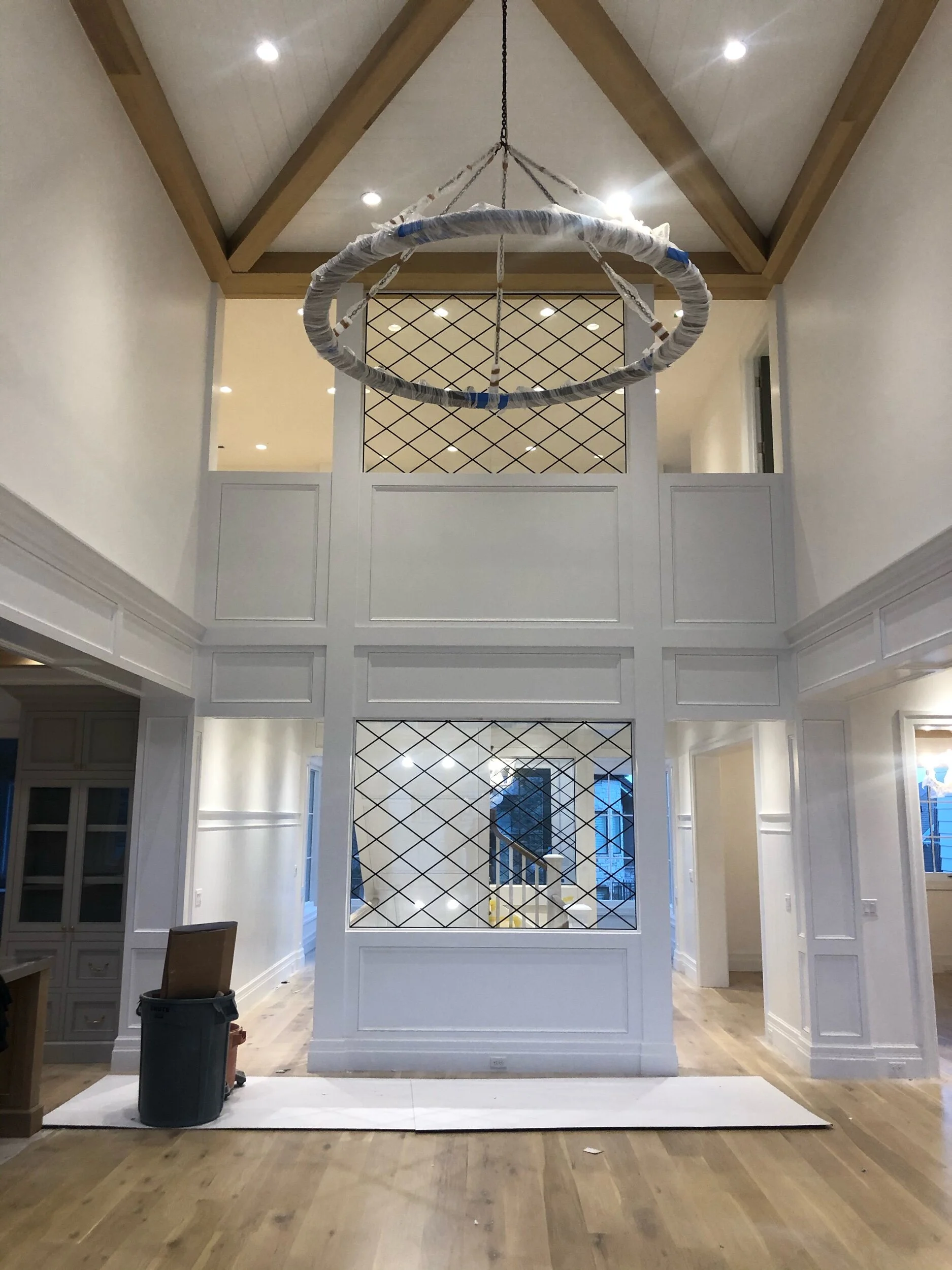 Interior room with a large white decorative divider featuring diamond-shaped lattice pattern, a hanging chandelier above, and wooden flooring.