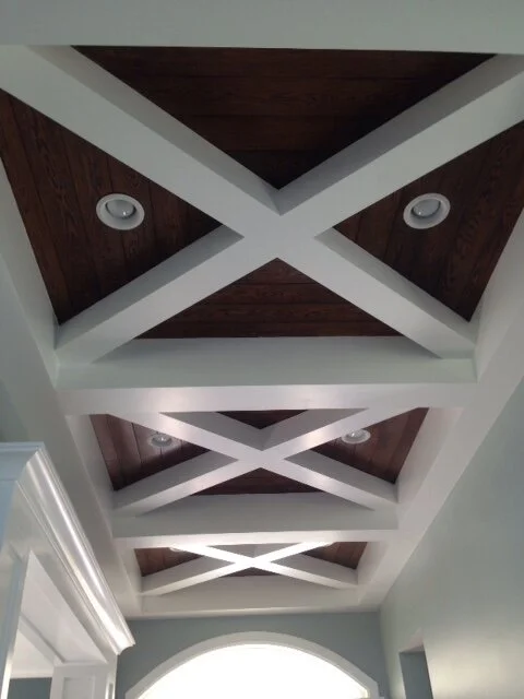 Ceiling with white beams forming an X pattern over a dark wood panel ceiling, with four recessed lights.