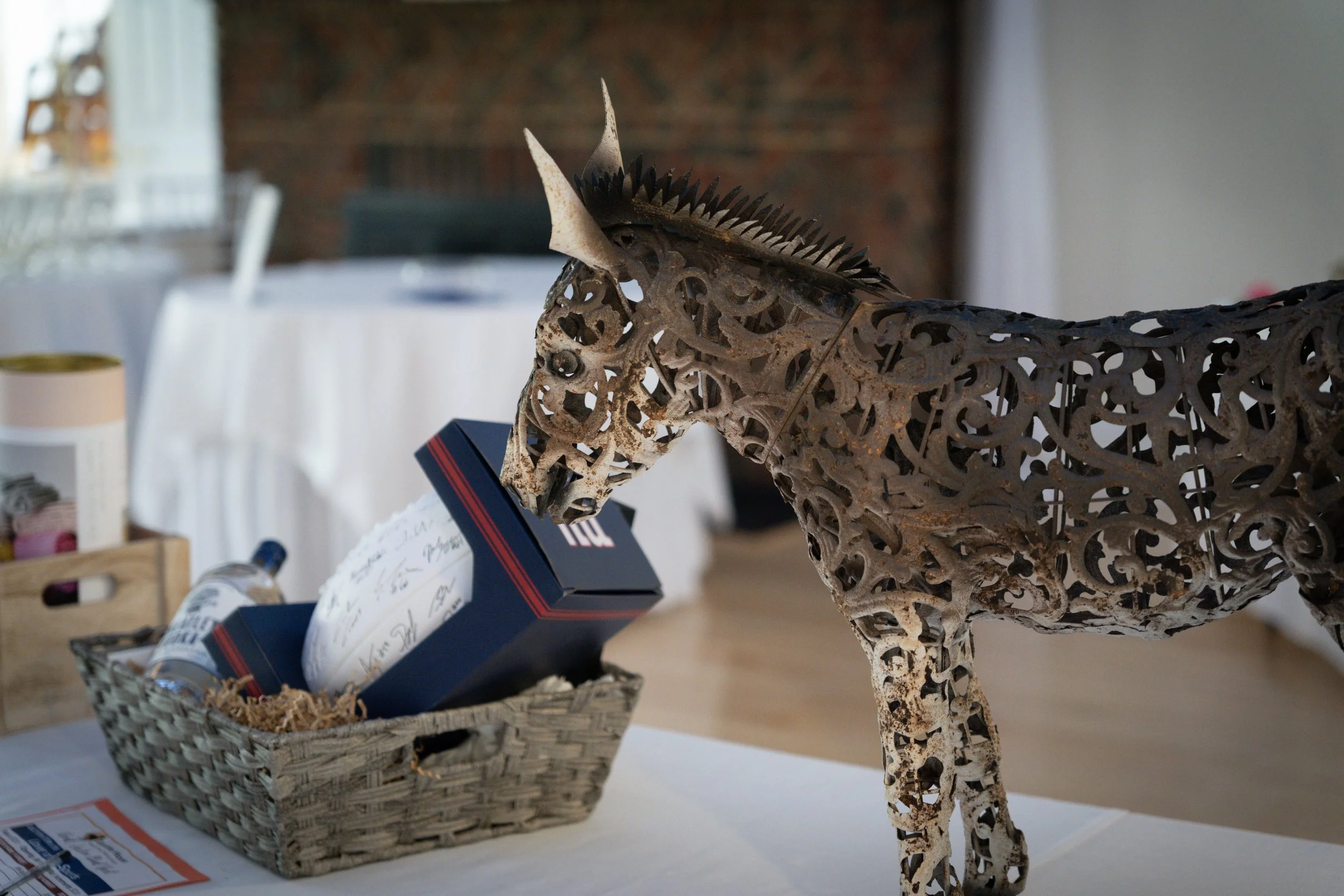 A decorative metal horse sculpture with intricate cut-out designs in a room with tables and a basket of items in the background.