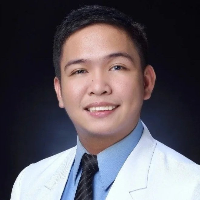 Smiling man in a white suit jacket, blue dress shirt, and black tie against a dark background