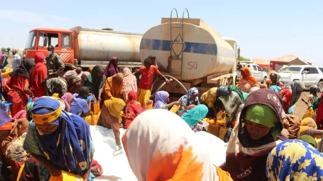 Crowd of people collecting water from a tanker truck in a crowded outdoor setting