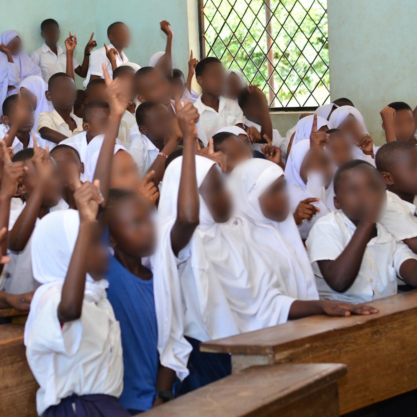 Students in white school uniforms raising their hands in a classroom