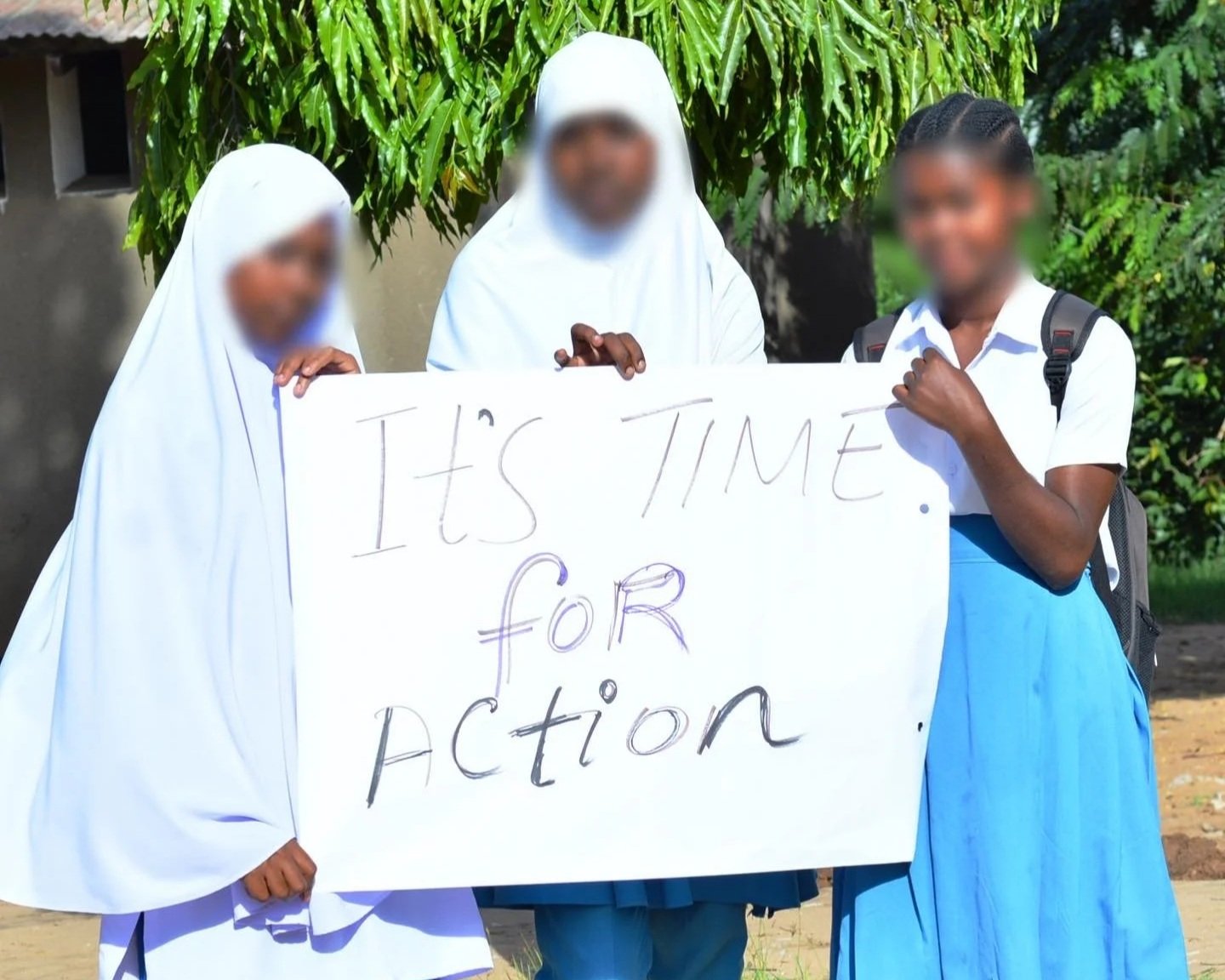 Three students holding a sign reading “It’s time for action” outdoors