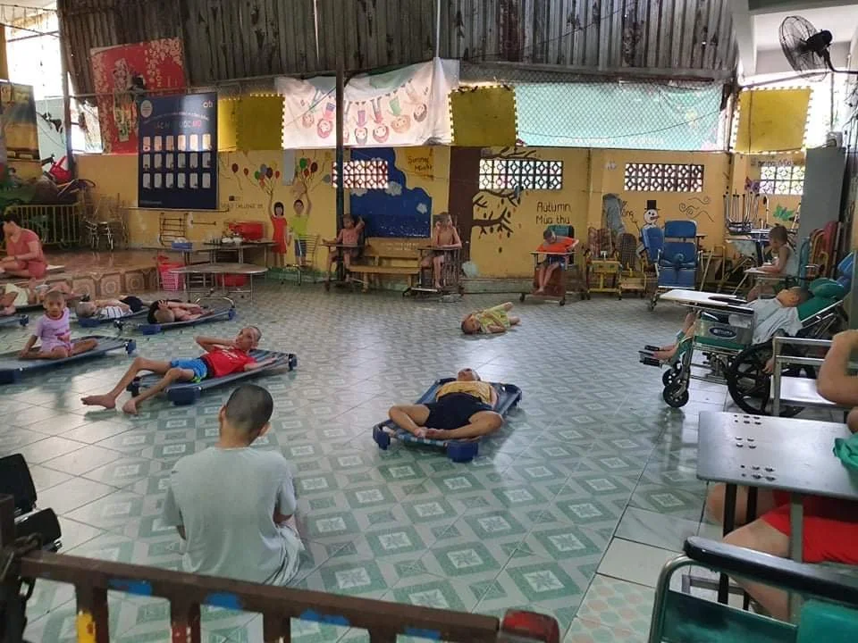Children and adults participating in physical therapy exercises on mats and adaptive equipment inside a colorful rehabilitation center