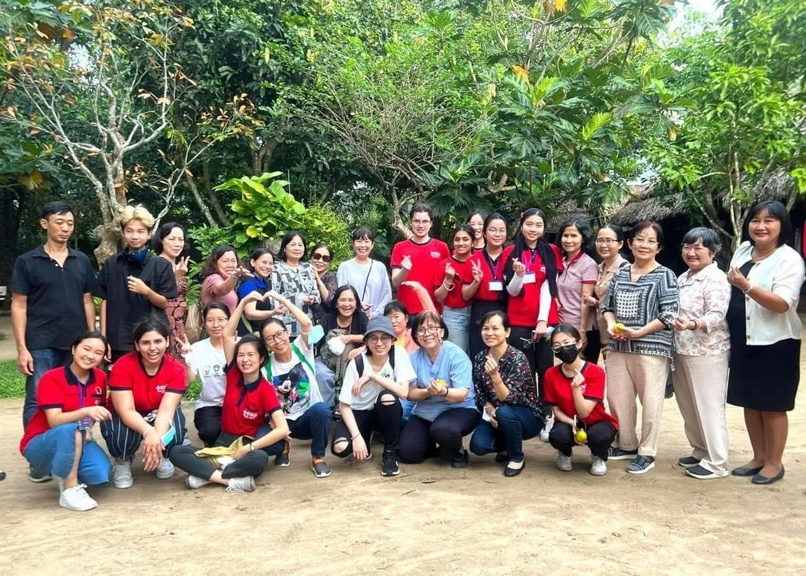 Large group of adults posing for a group photo outdoors in a lush tropical garden