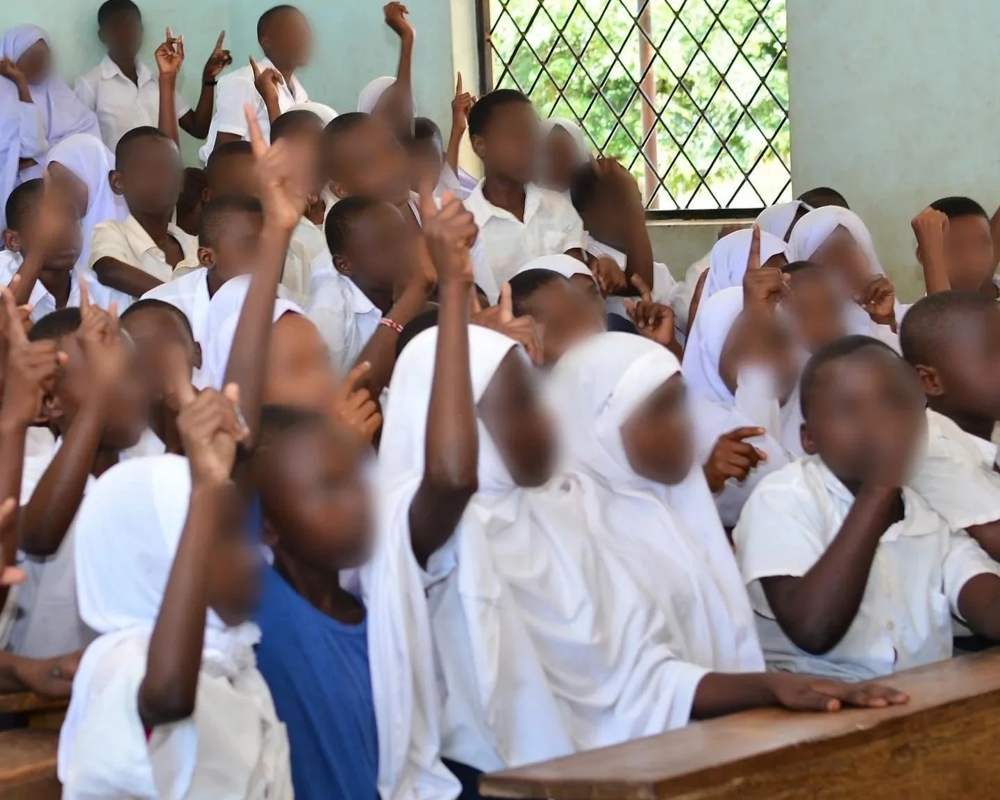 Students in white school uniforms raising their hands in a classroom