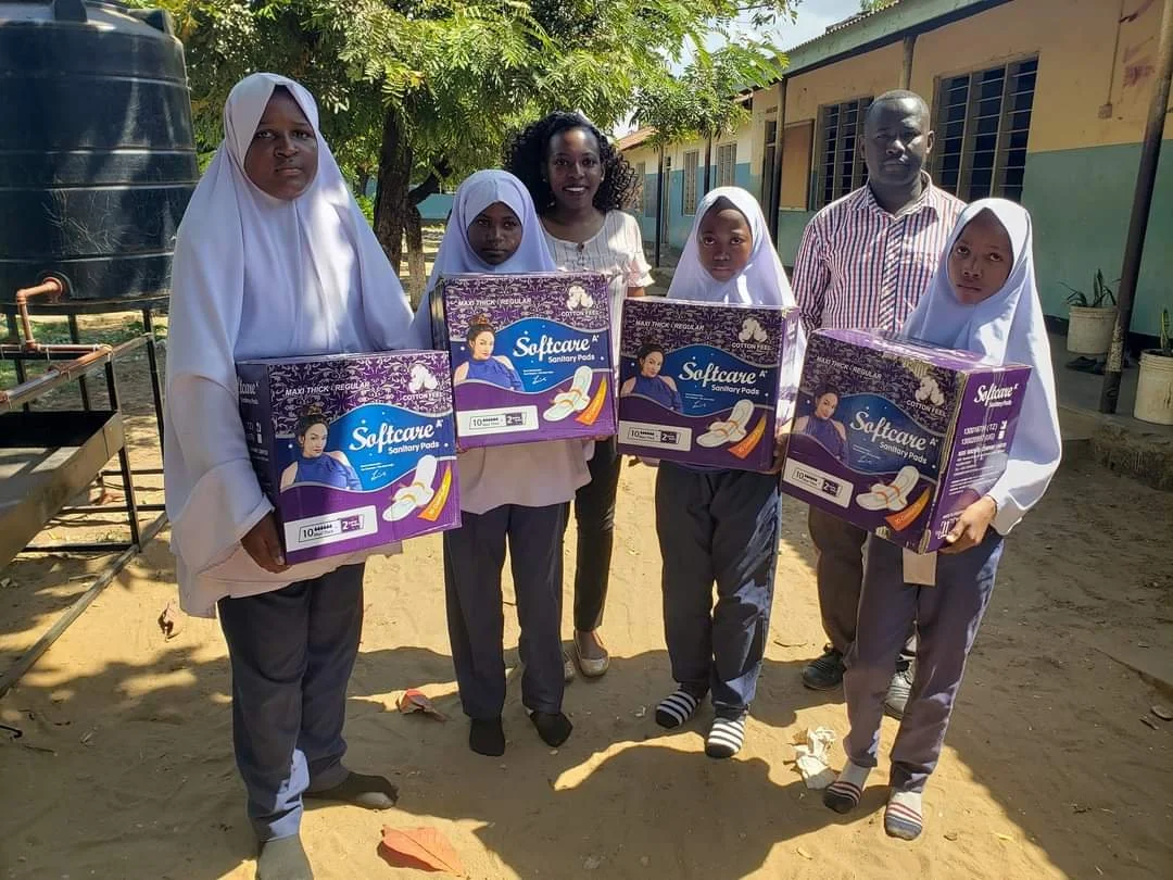 Schoolgirls and adults holding boxes of Softcare sanitary pads outside a school building