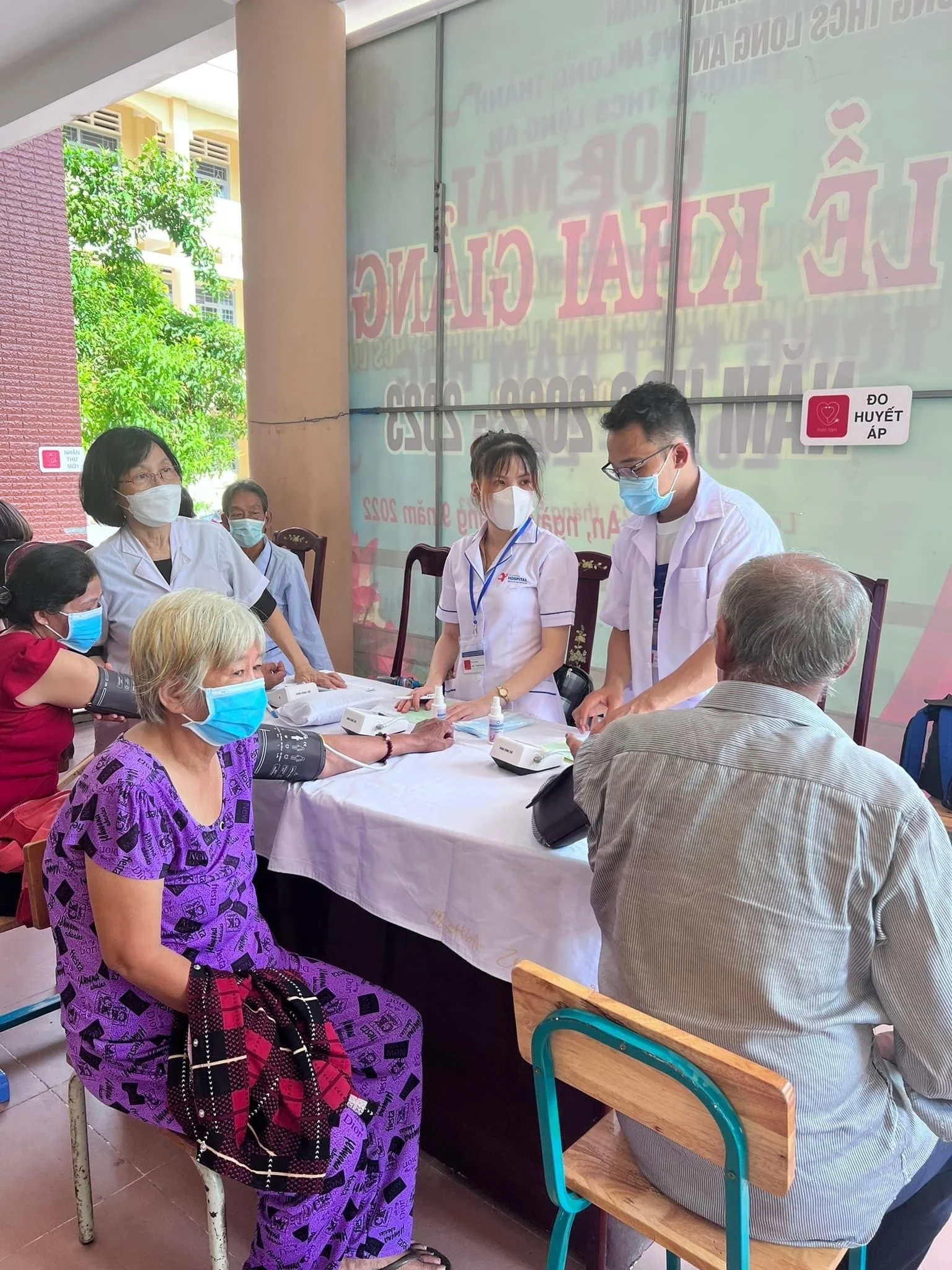 Masked healthcare workers check patients’ blood pressure at a community health screening table.