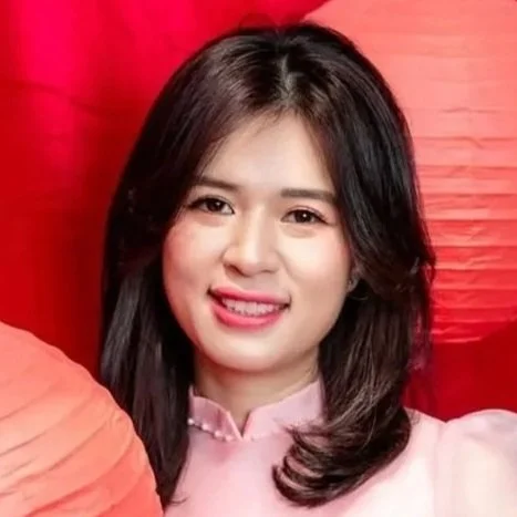Smiling woman with shoulder-length dark hair wearing a pink blouse against a red background