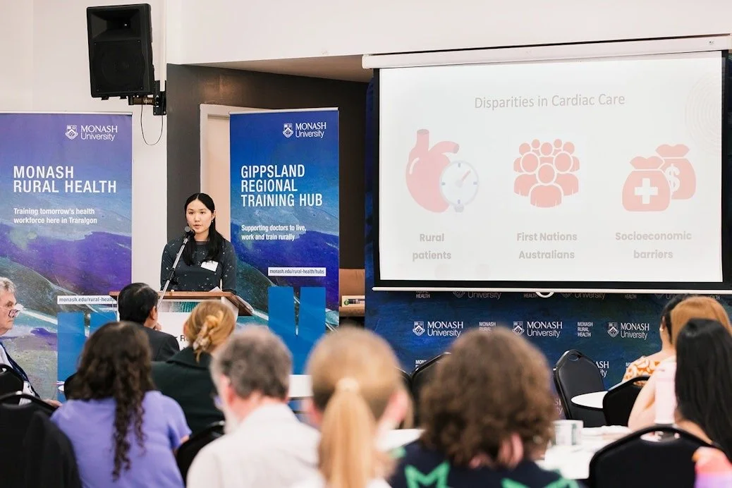 Monash University rural health presentation on disparities in cardiac care, with speaker at podium and seated audience