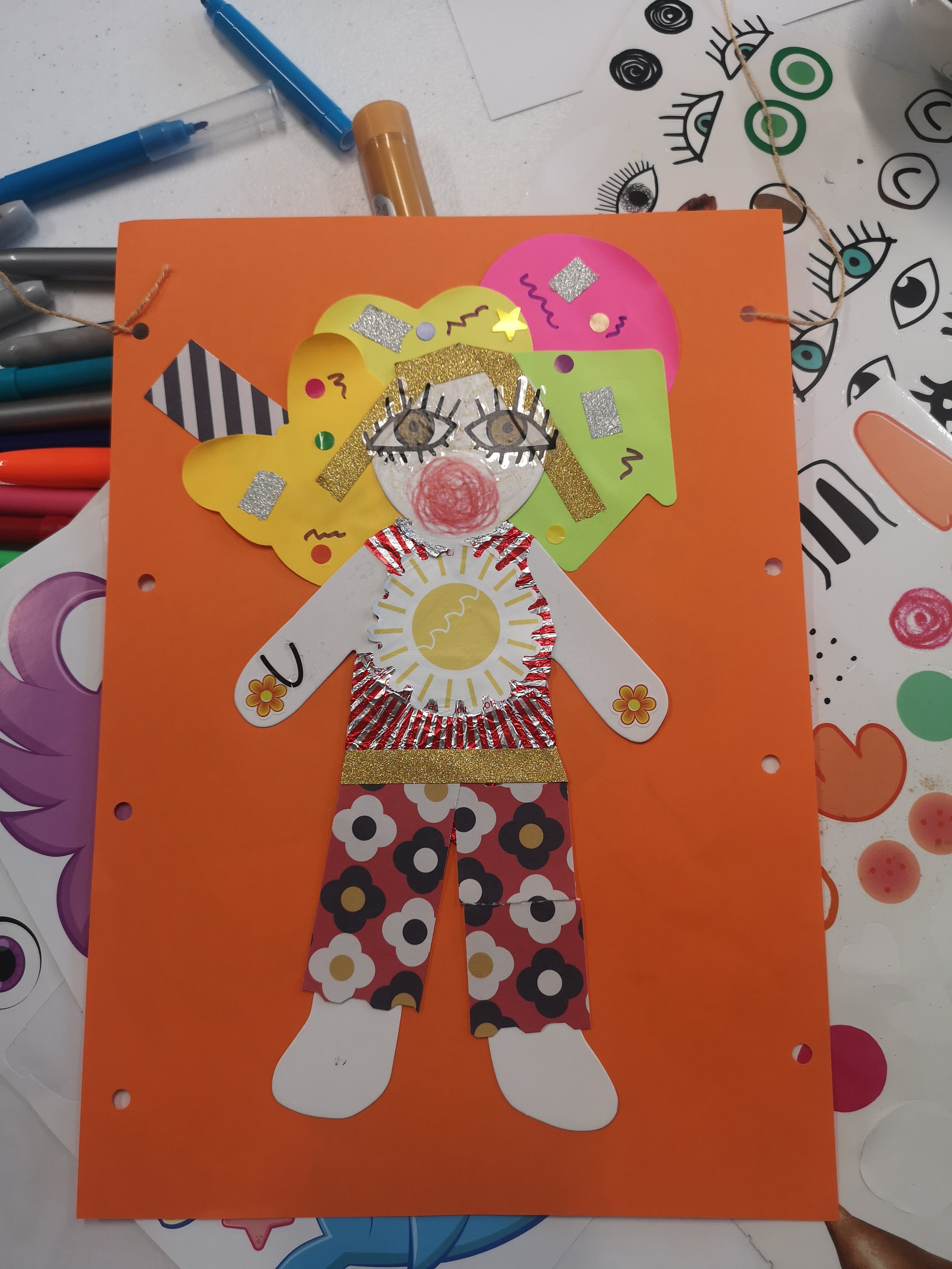 A anon on a orange background with patterned trousers and a flower top.