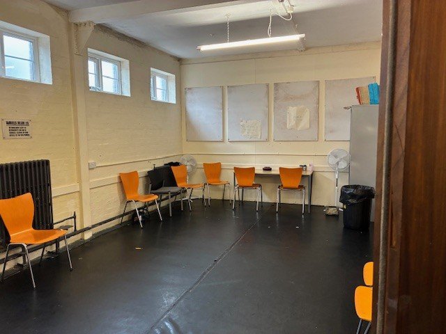 bare room with black flooring and a yellow brick wall. There are orange chairs round the edges.