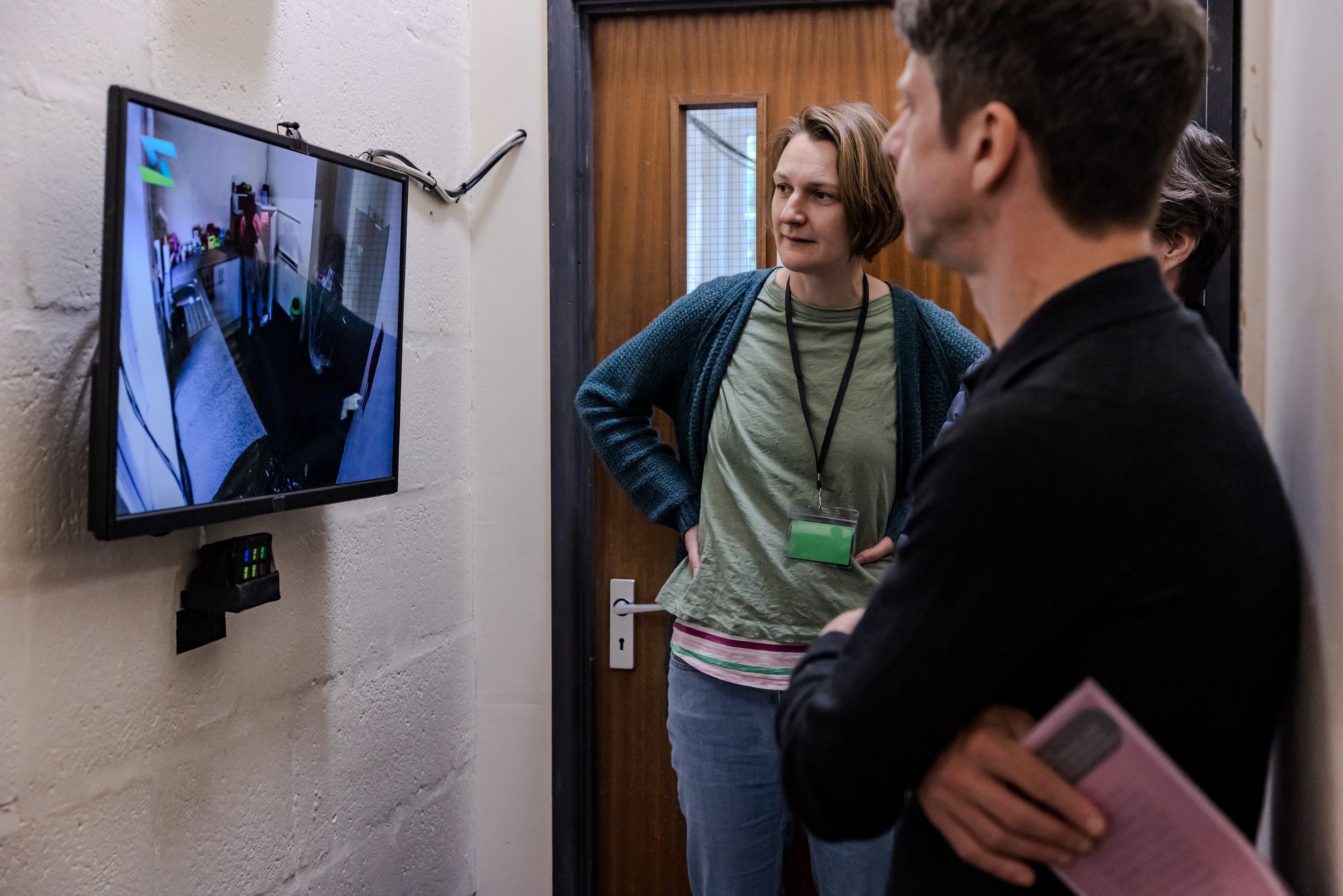 Two audience members look confusingly at a screen depicting a messy kitchen with someone opening the fridge
