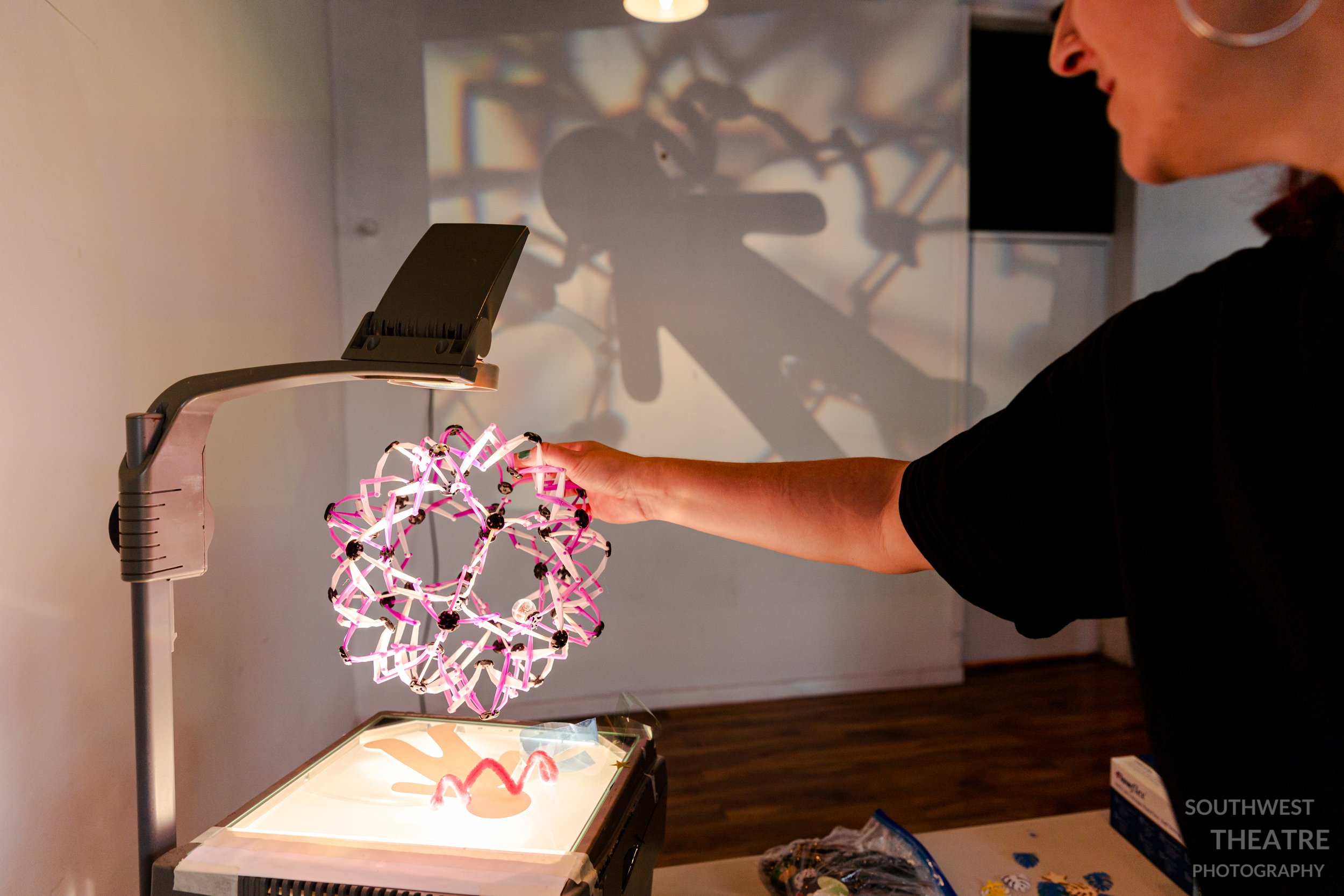 Some one holding a toy over a overhead projector with a anon below. It creates complex shadows on the far wall