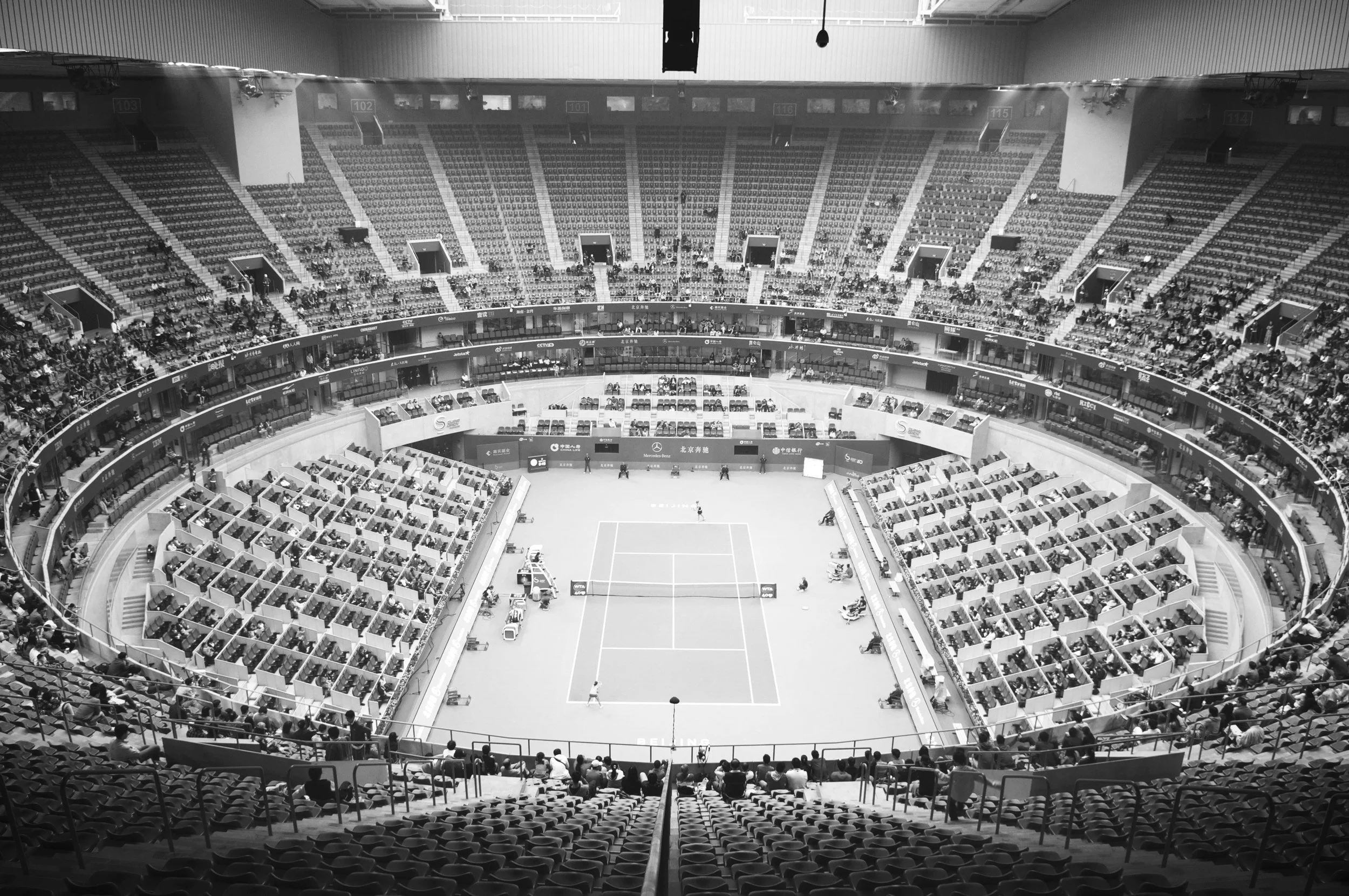 An indoor tennis stadium with a central court and tiered seating filled with spectators.