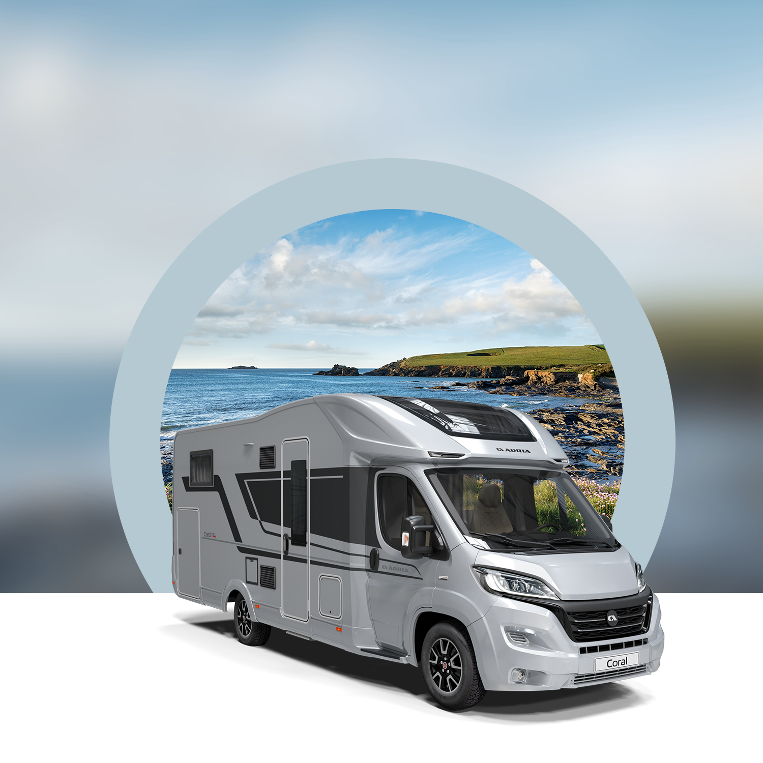 A gray recreational vehicle (RV) parked in front of a circular backdrop showing a coastal landscape with blue sky and clouds.